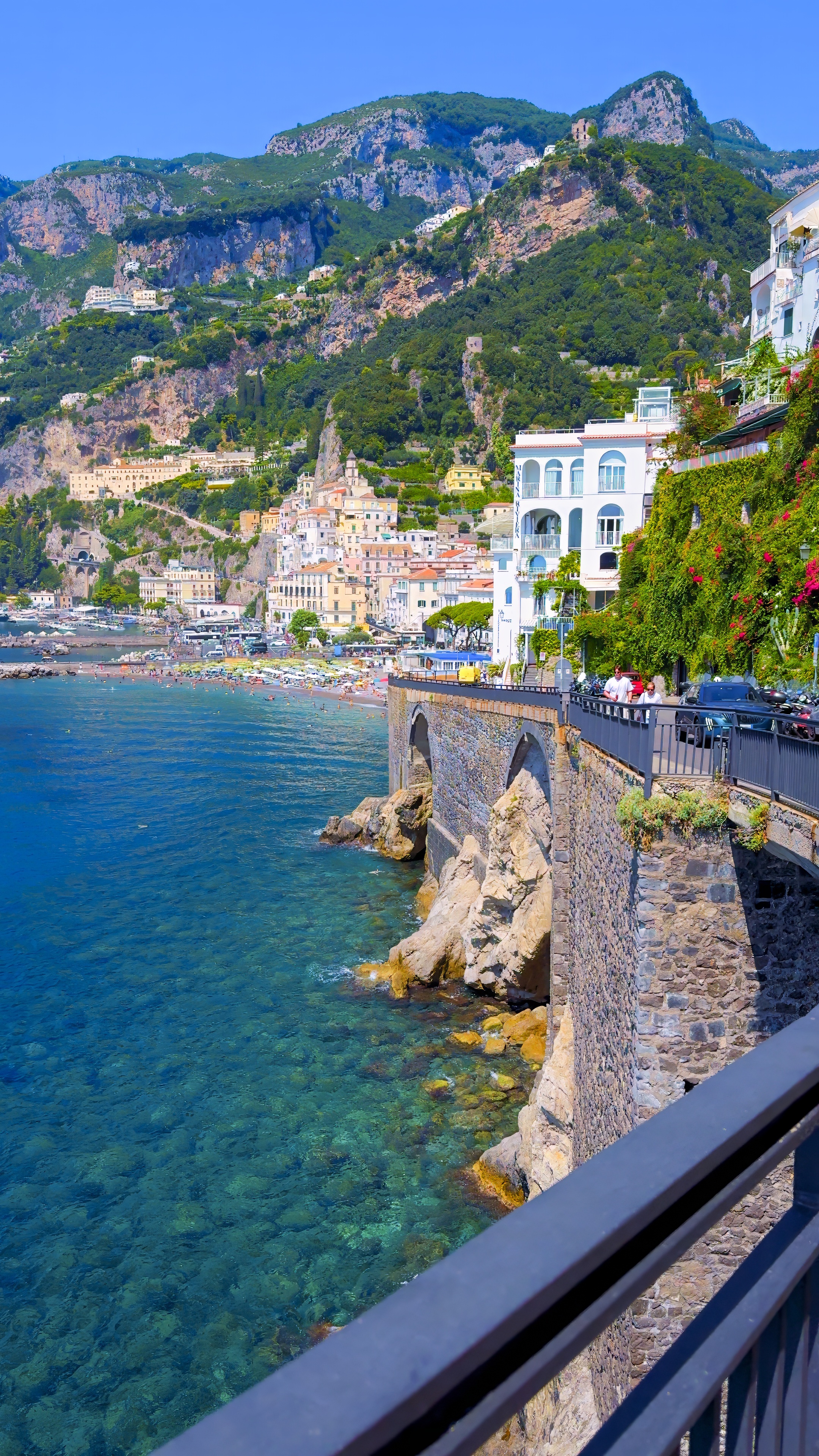 A coastal town at dusk seen from a balcony, with rocks and clear water below