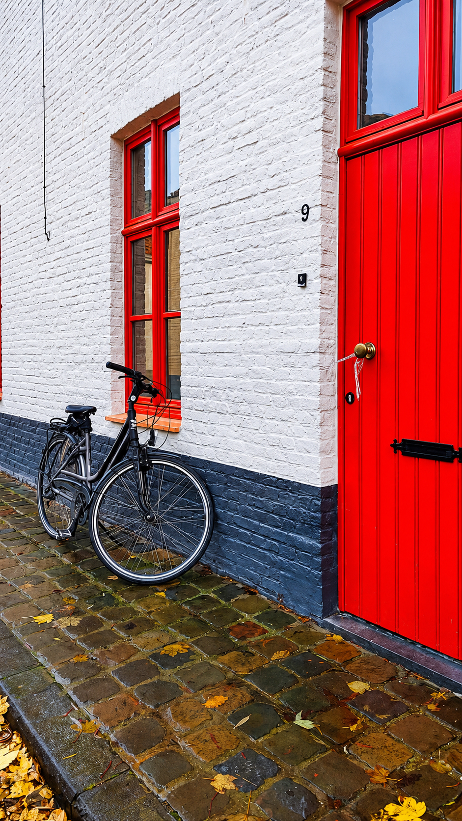 A bicycle against a whitewashed house with a red door and red window frames