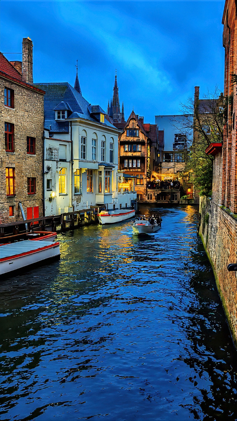 A Bruges canal lined with brick and painted houses, with open boats moored along the bank.