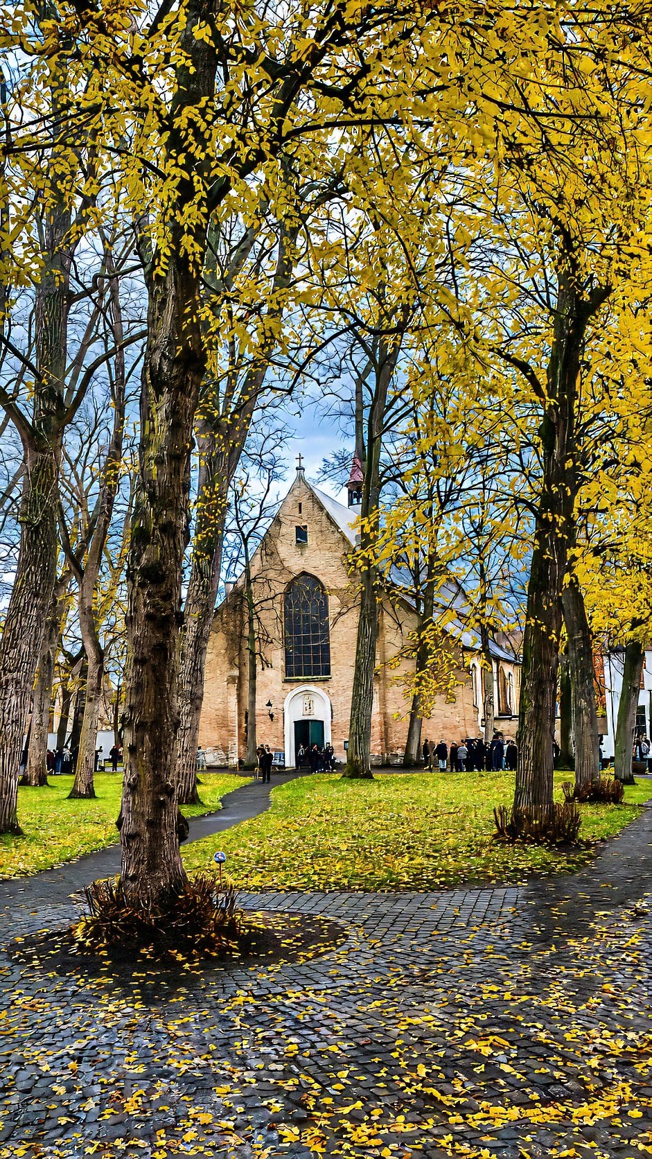 A leaf-covered path under autumn trees, with a brick church behind.