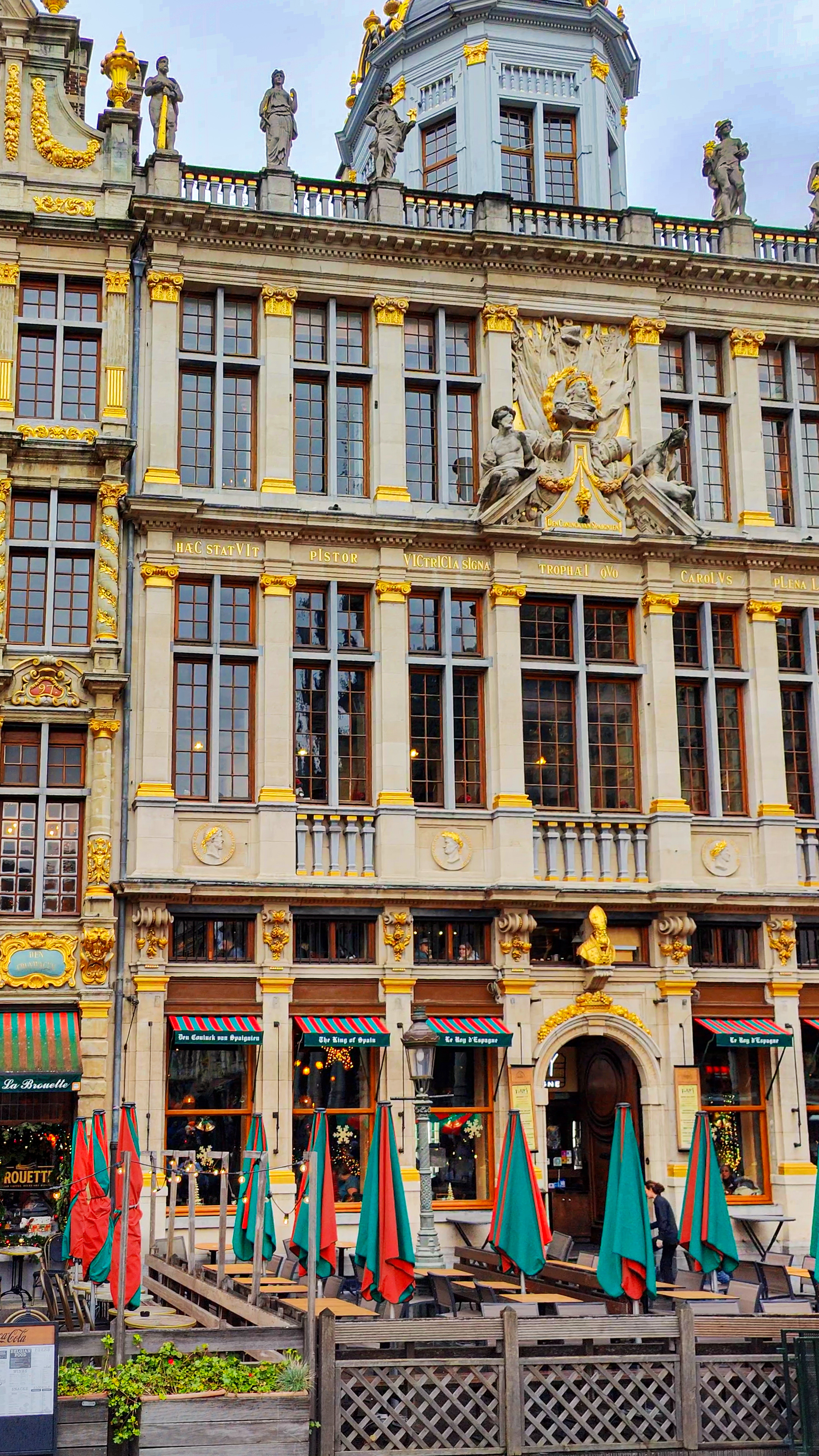 A gilded guild house on the Grand-Place in daylight, with café umbrellas below.