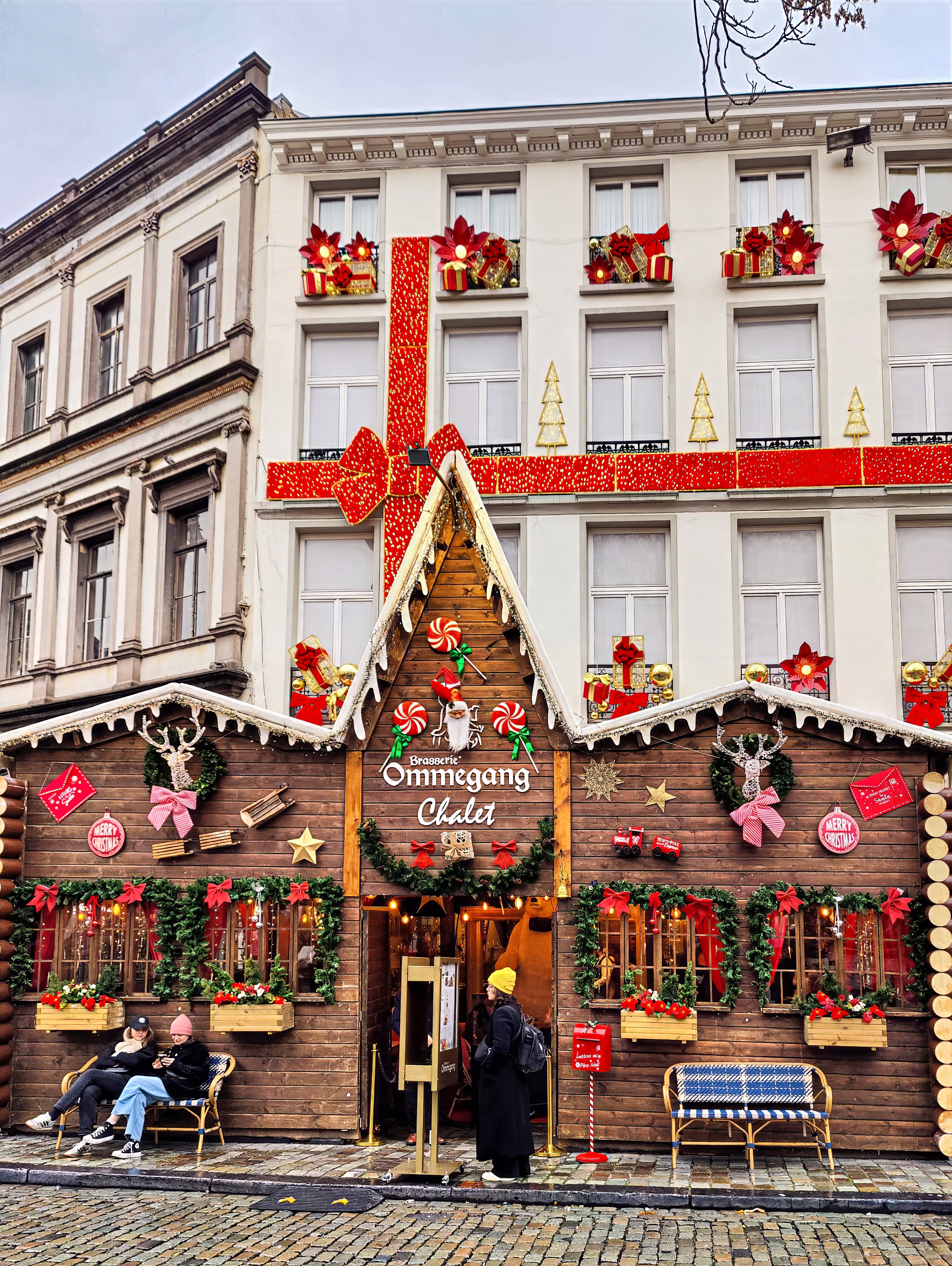 A building decorated for Christmas with red ribbons and garlands above a wooden chalet-style shopfront.
