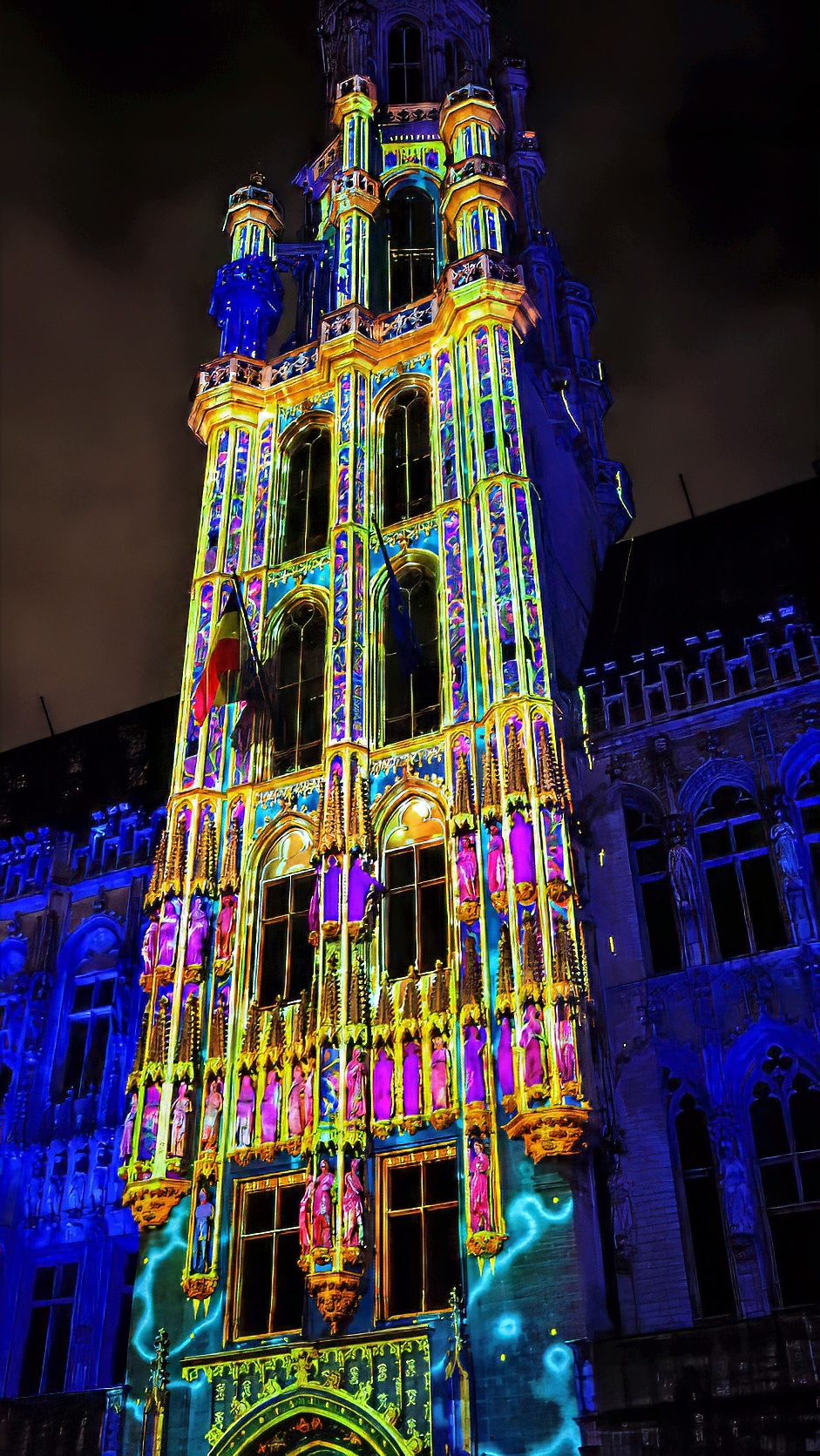 The Town Hall tower on the Grand-Place covered in a coloured light projection at night.