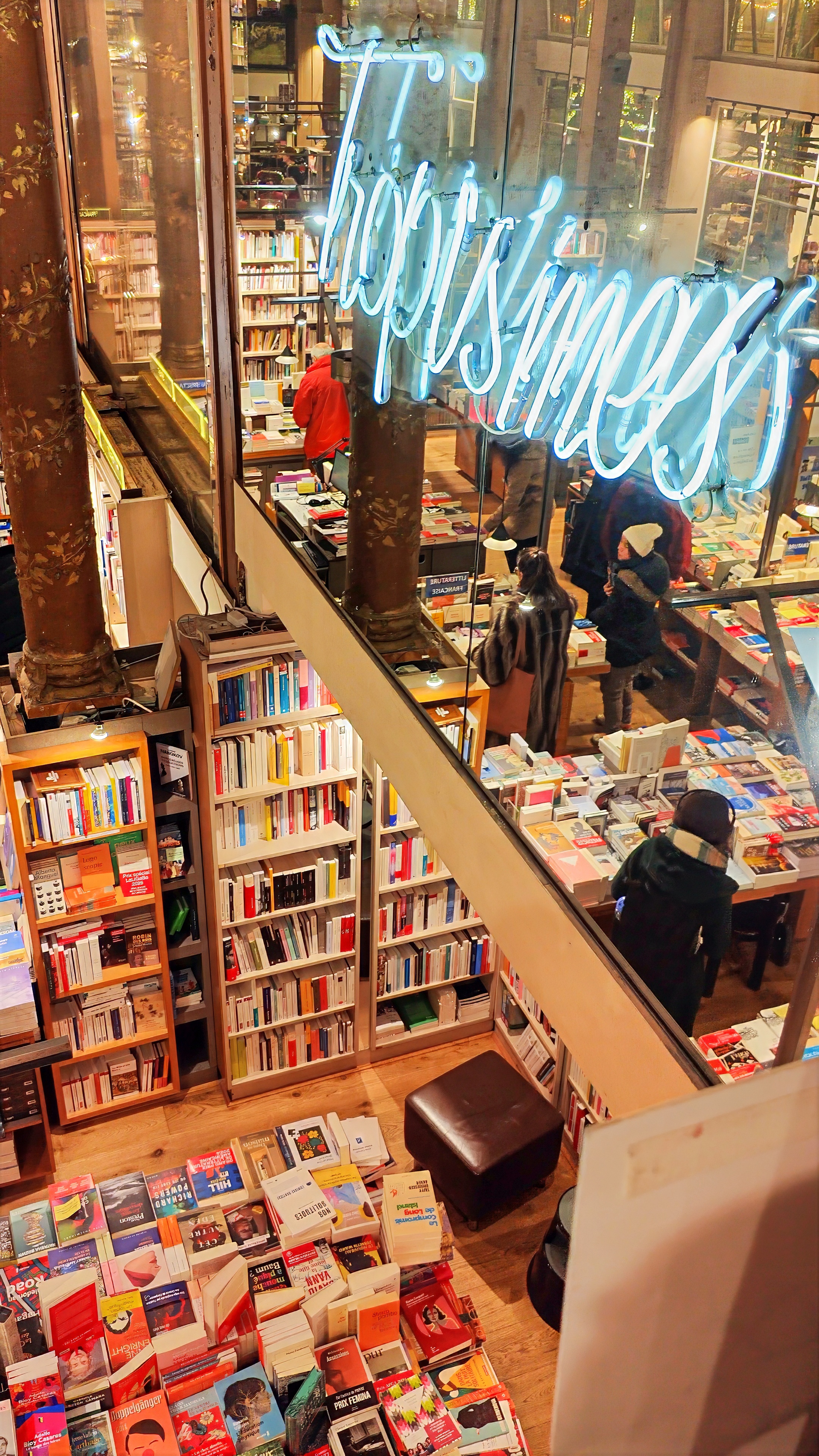 A bookshop beneath the covered galleries, seen from above, with a neon sign over the shelves.
