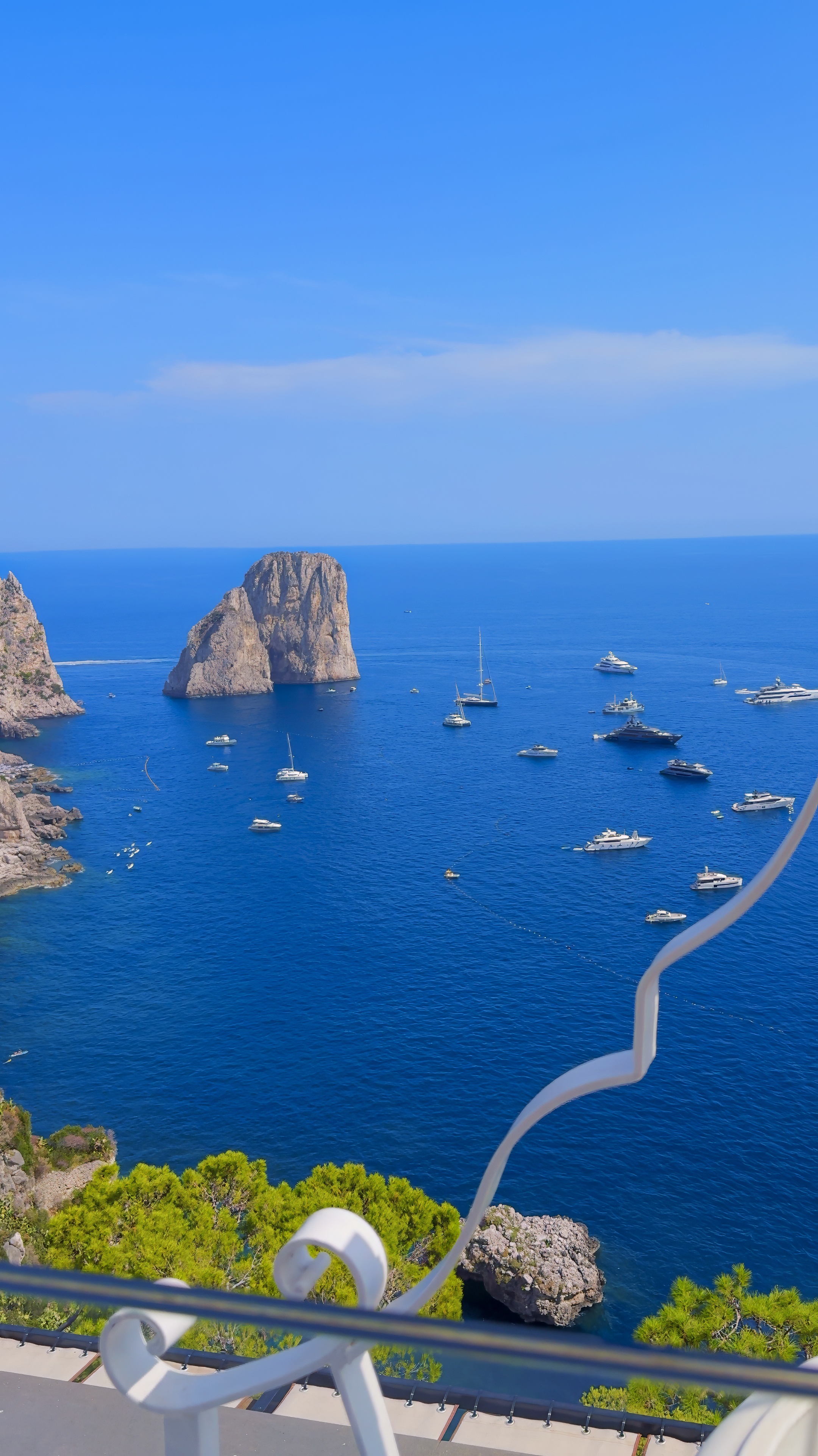 The Faraglioni seen from high above, with boats scattered across the blue water.