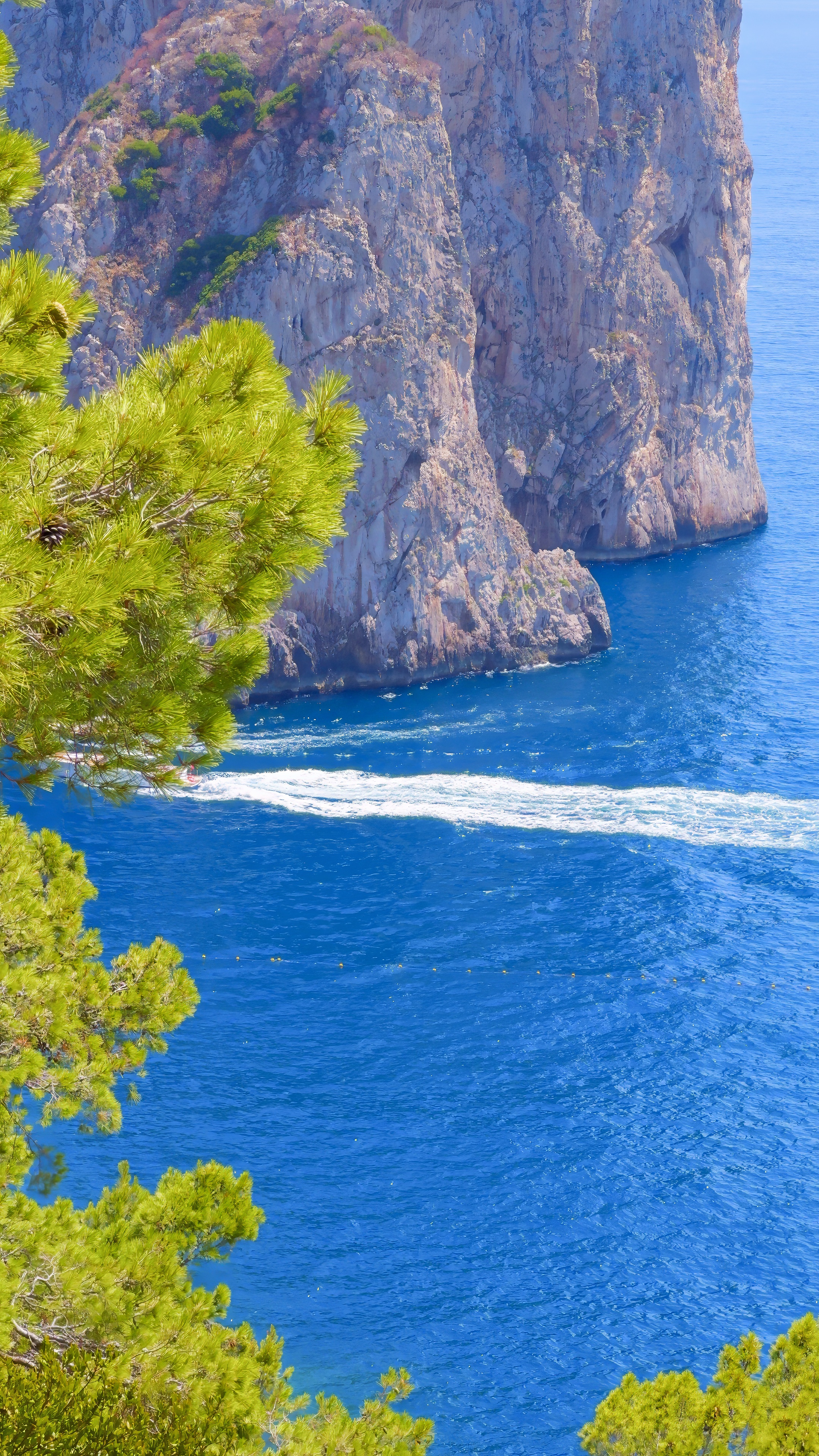 A close view of the Faraglioni rock faces, with the wake of a boat below.