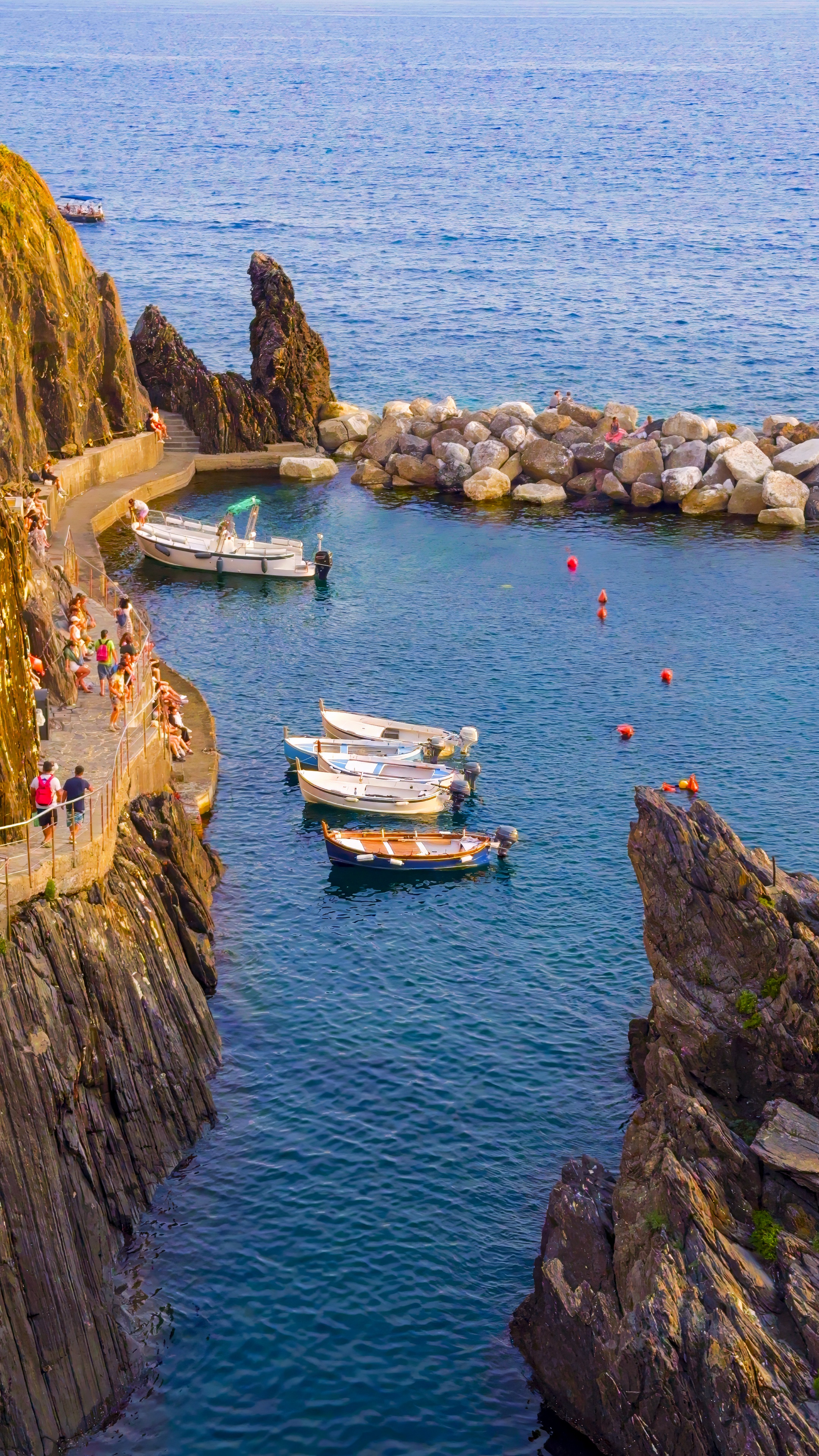 A narrow rocky inlet with small boats moored in clear blue water.