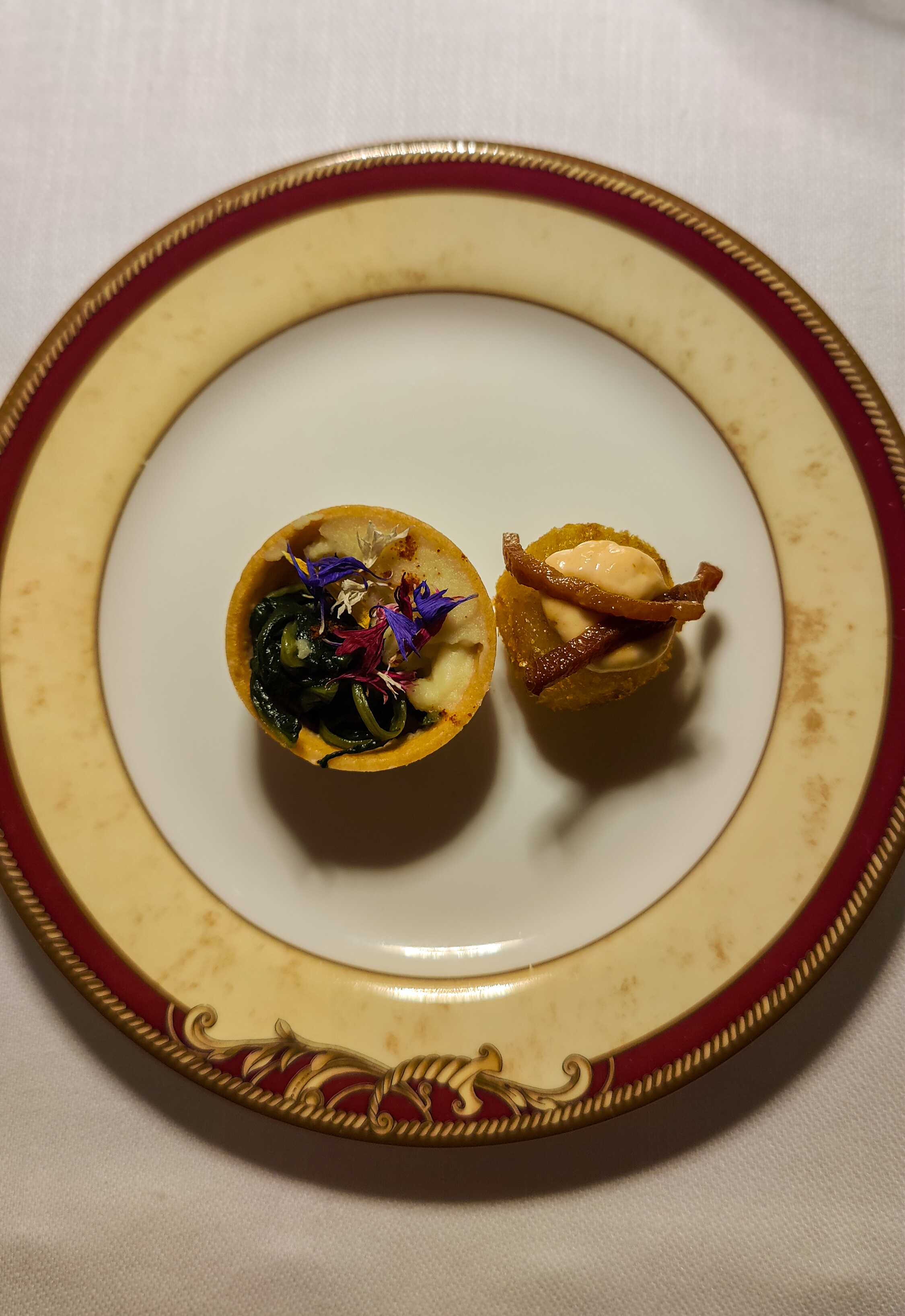 Two small bites on a white plate with a wide gold and burgundy rim