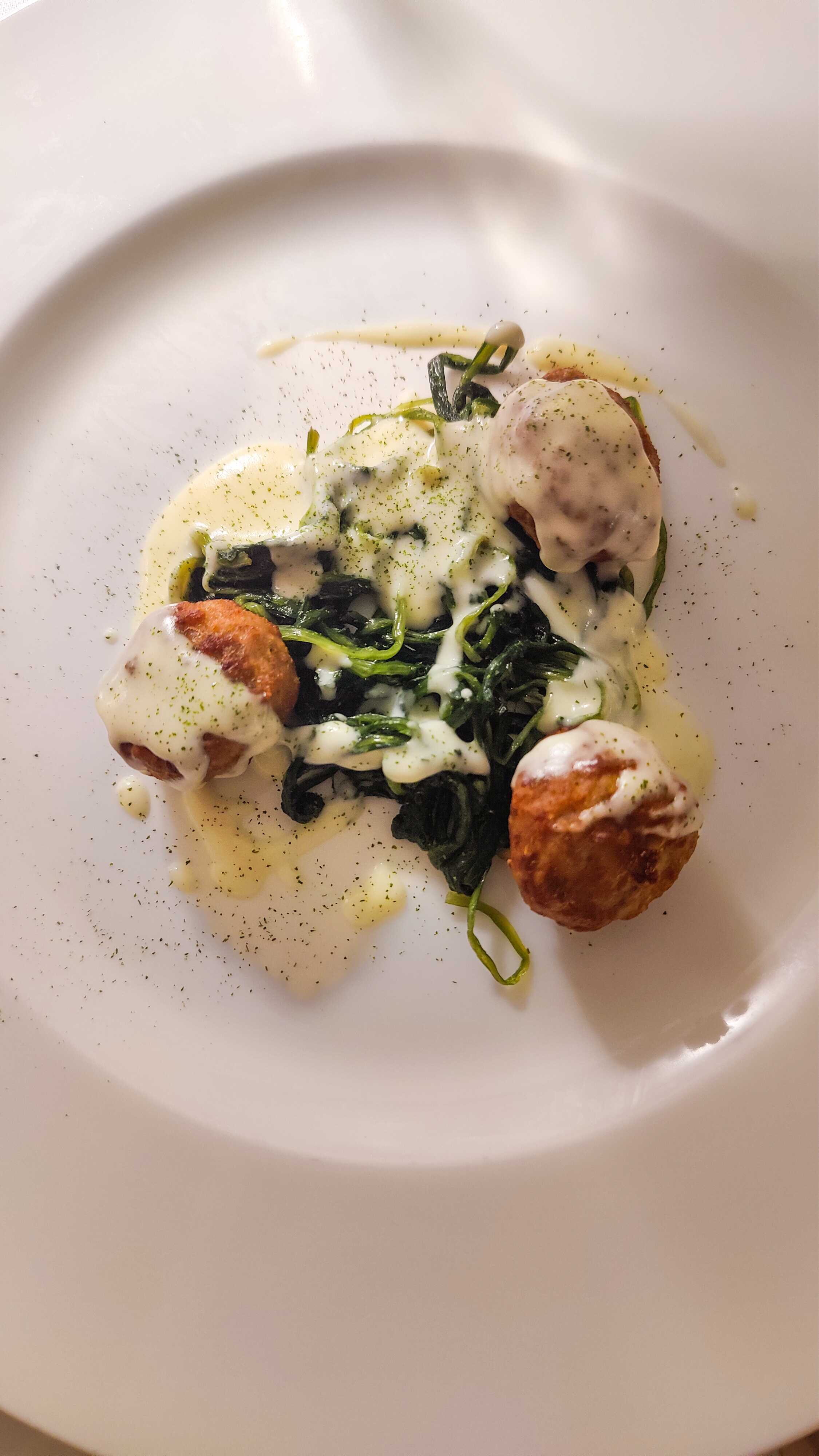 A composed dish with wild greens in a pale sauce on a white plate