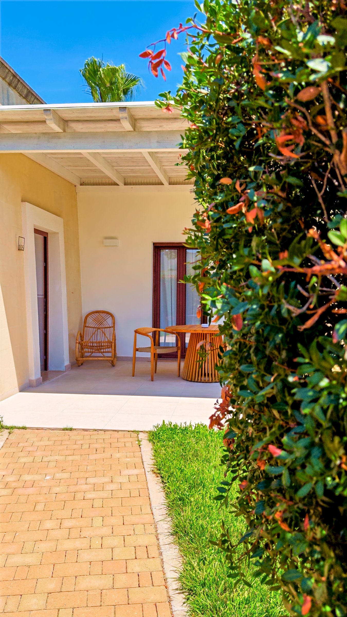 The covered veranda outside our room, with a table and chairs, a brick path and bougainvillea in flower