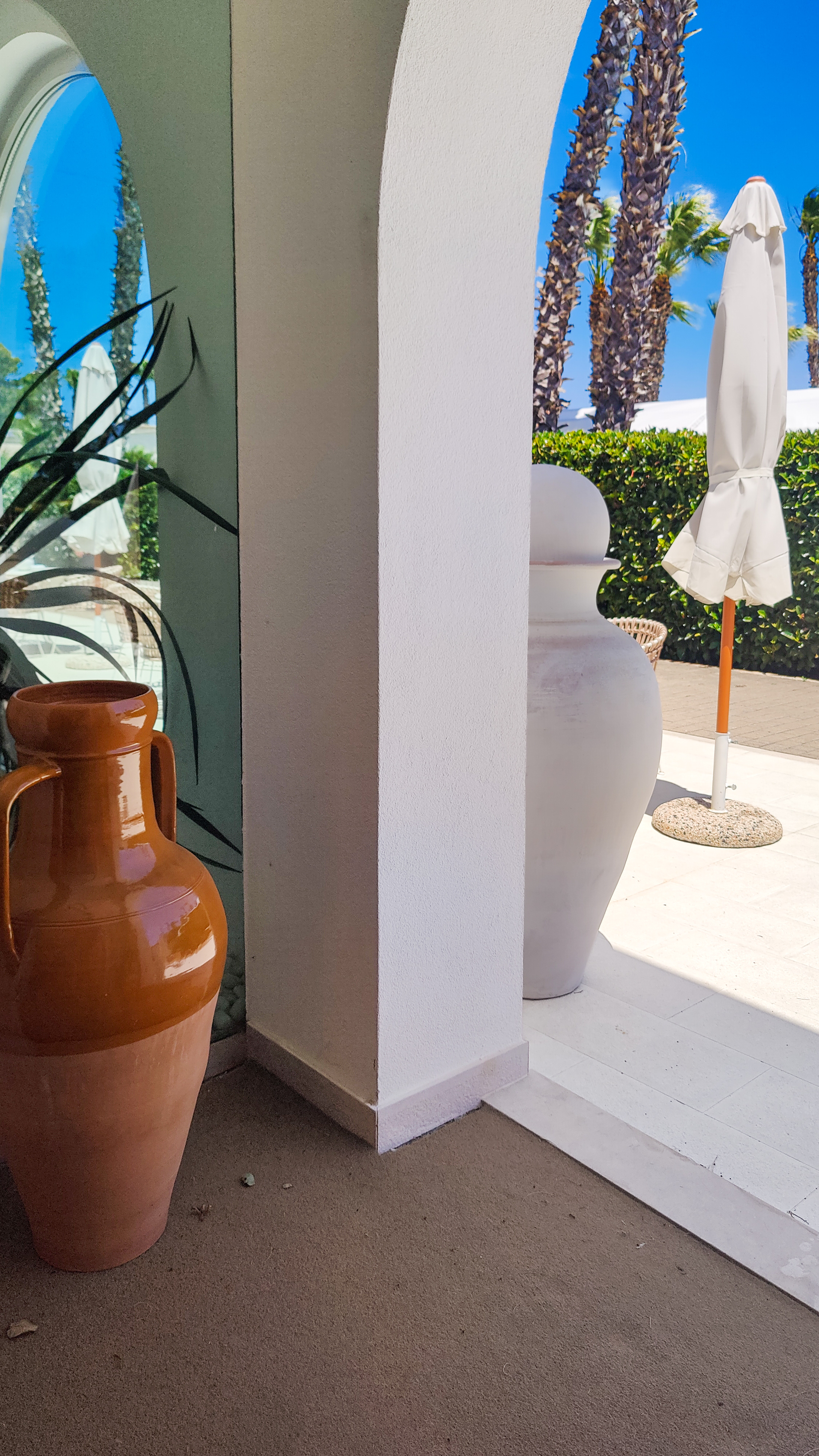 A terracotta urn beside a white arch on a sunlit terrace