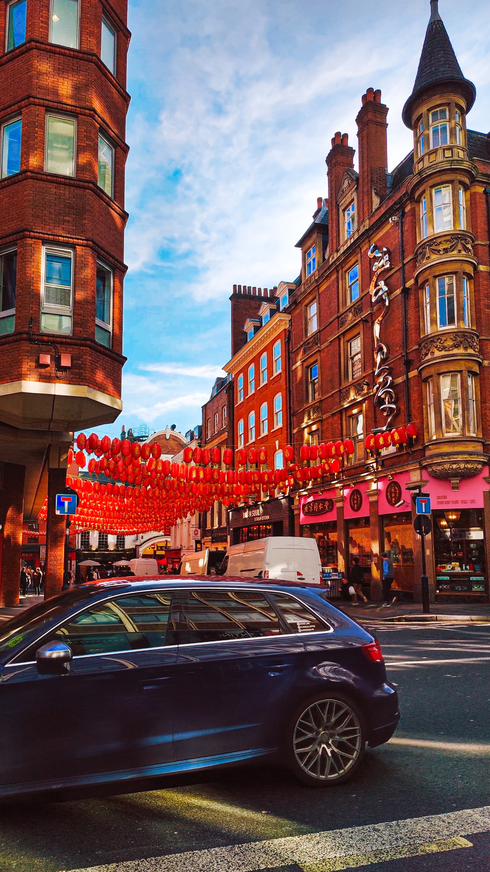 Red lanterns strung across a street of red-brick buildings, with a car passing below.