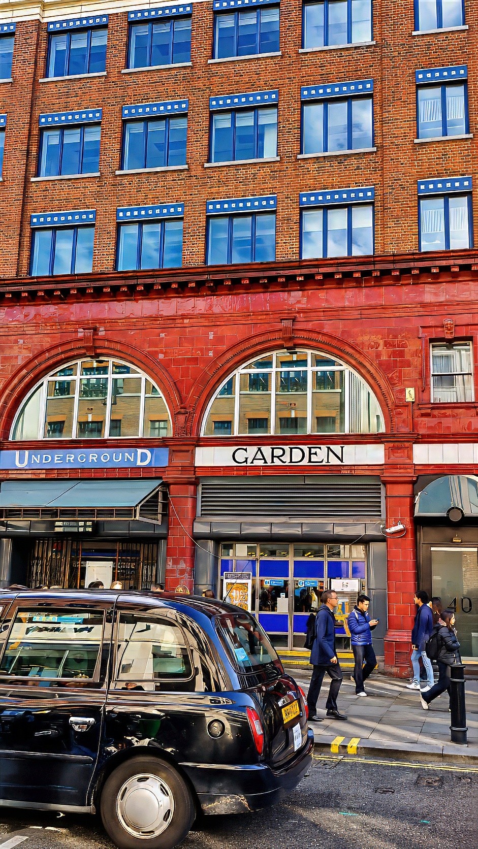 A black taxi in front of a red-brick Underground station with Covent Garden lettering above the entrance.