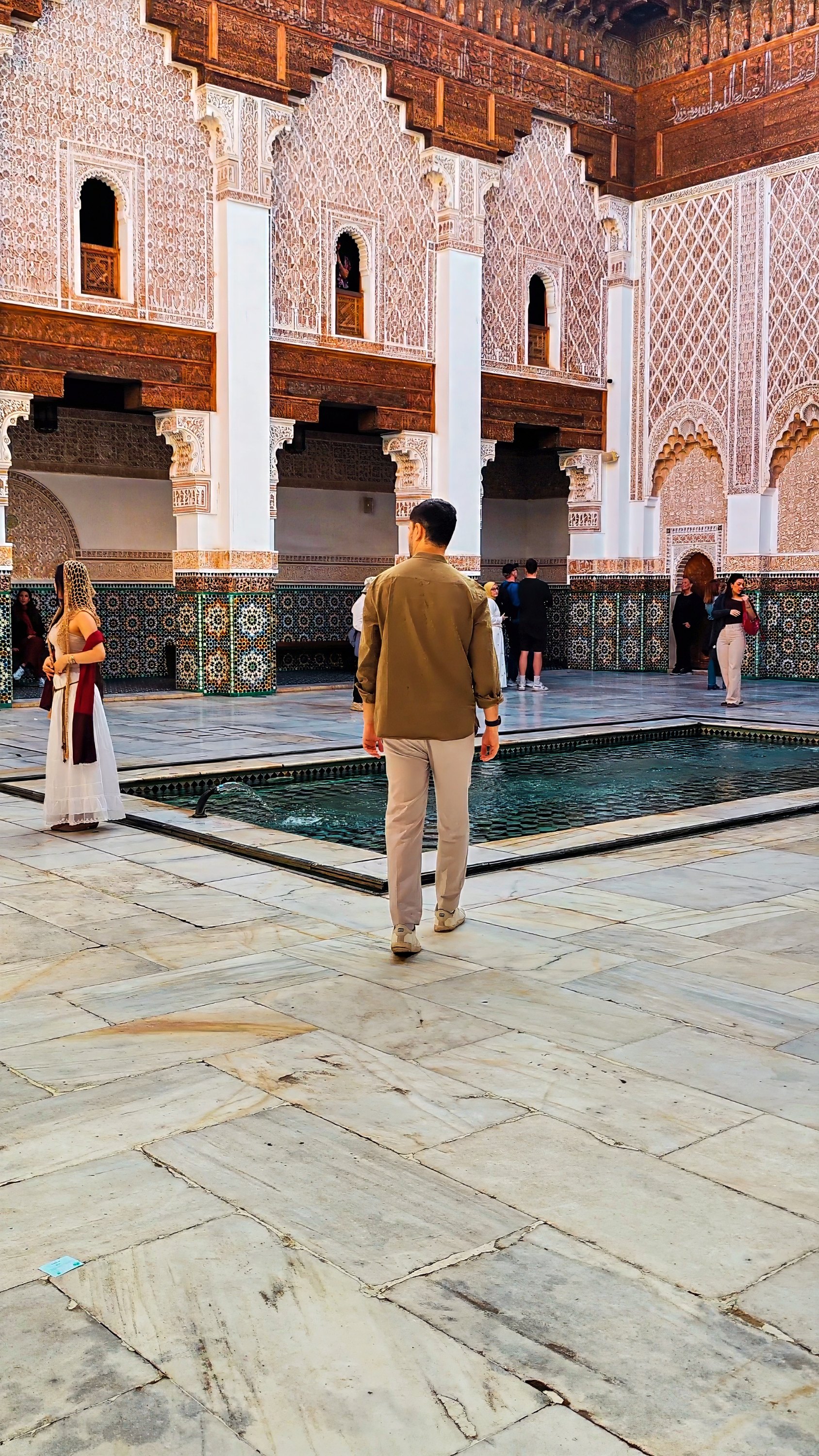 Barbara and Davide in a courtyard of carved stucco, cedar and zellige around a long reflecting pool.