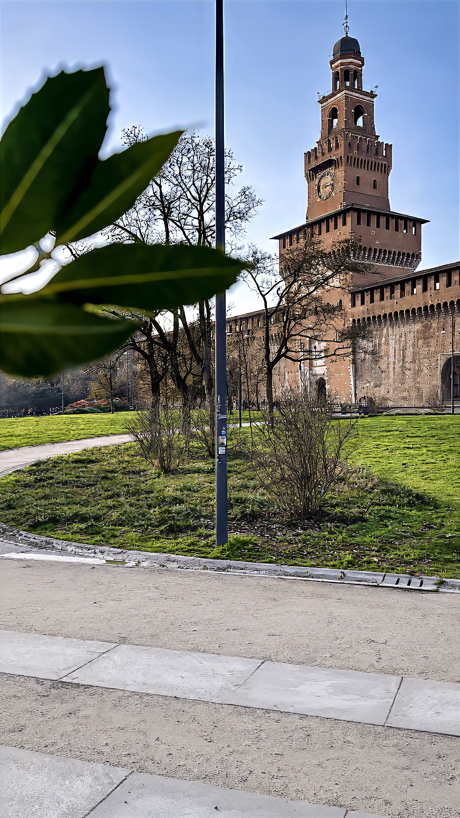 The brick gate tower of the Castello Sforzesco above a lawn and a paved path.