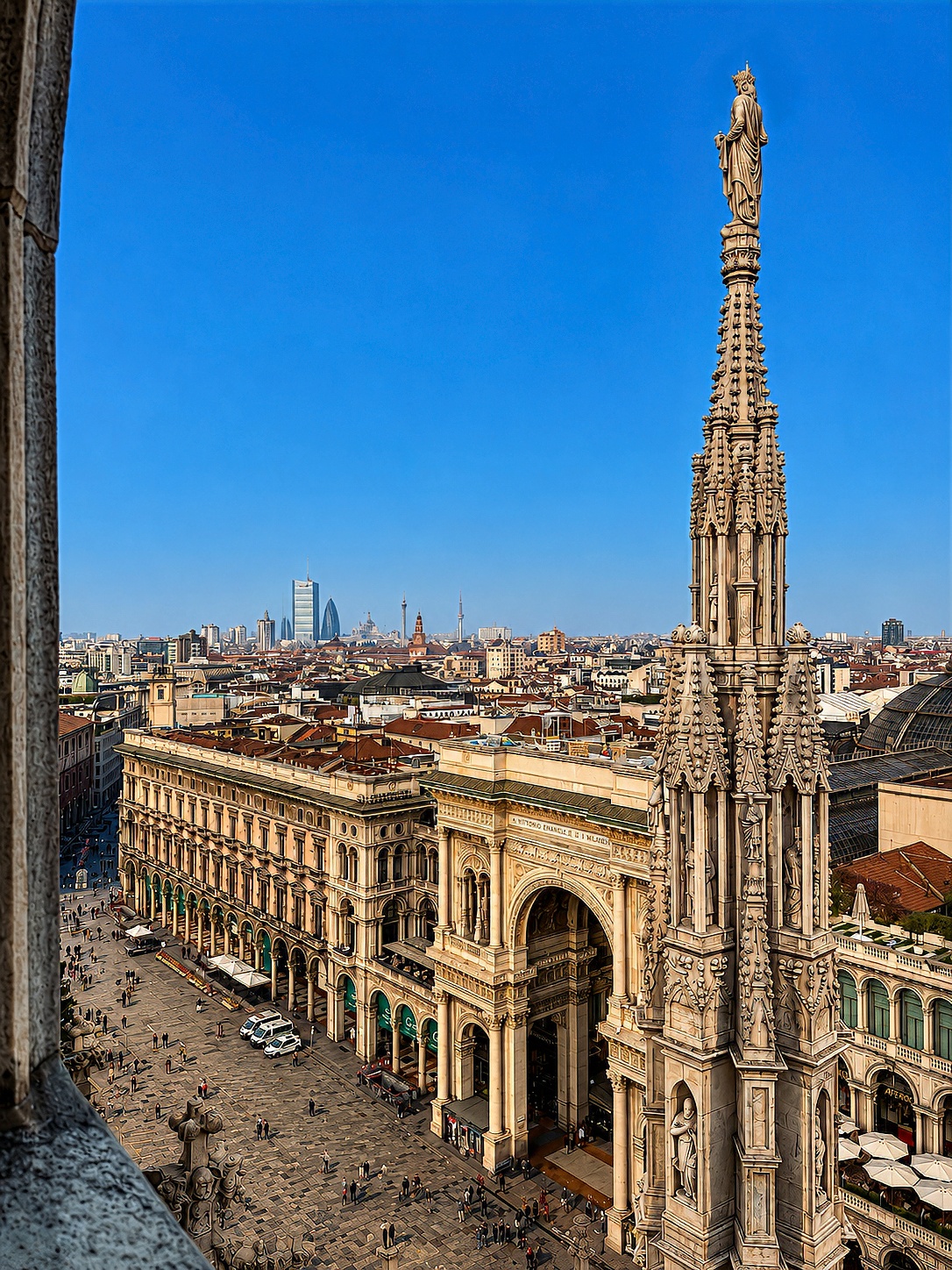 The piazza and the entrance arch of the Galleria seen from the cathedral roof, beside a marble spire.