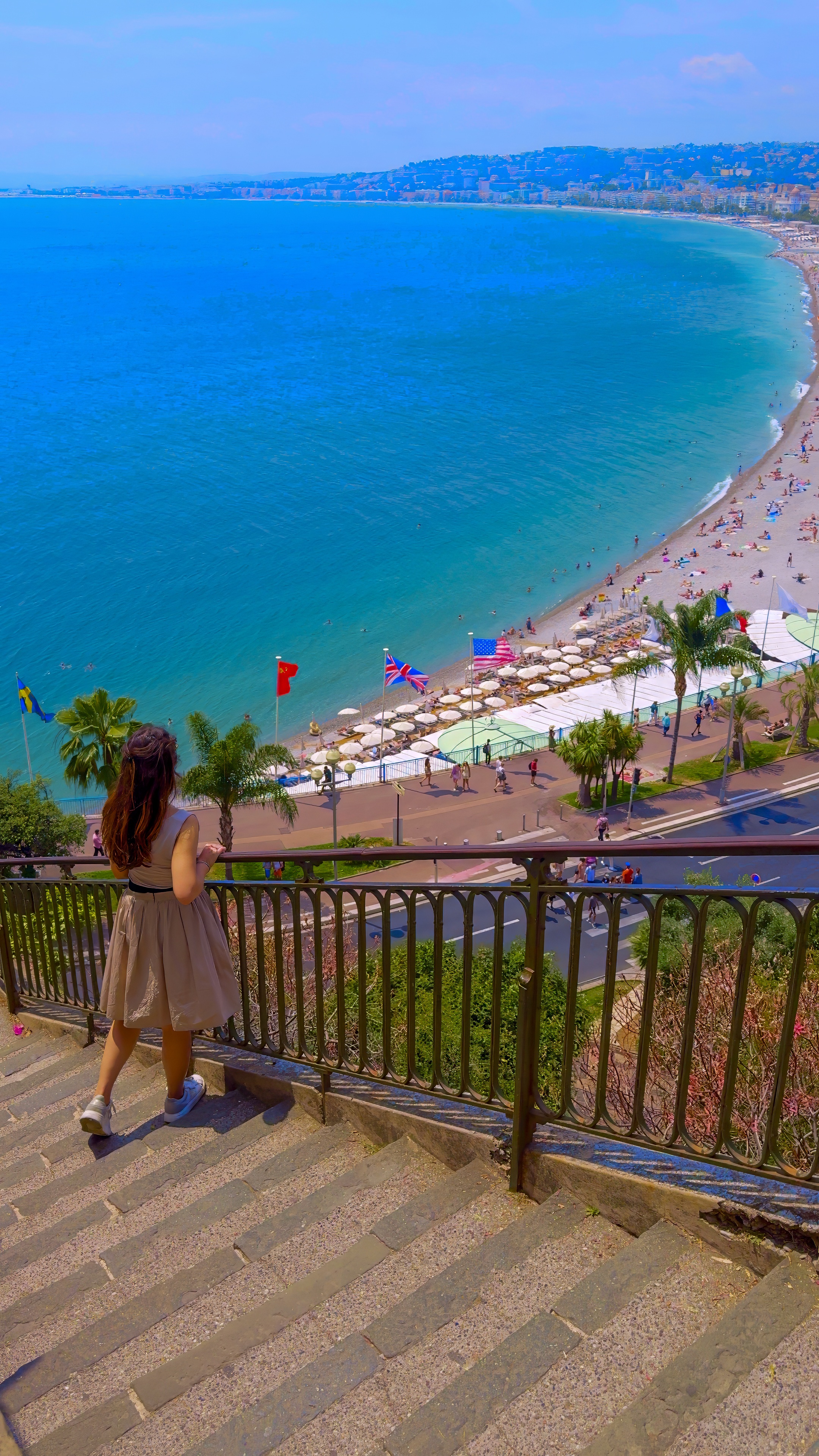 Barbara on stone steps beside a railing, above the curve of the bay and the beach.