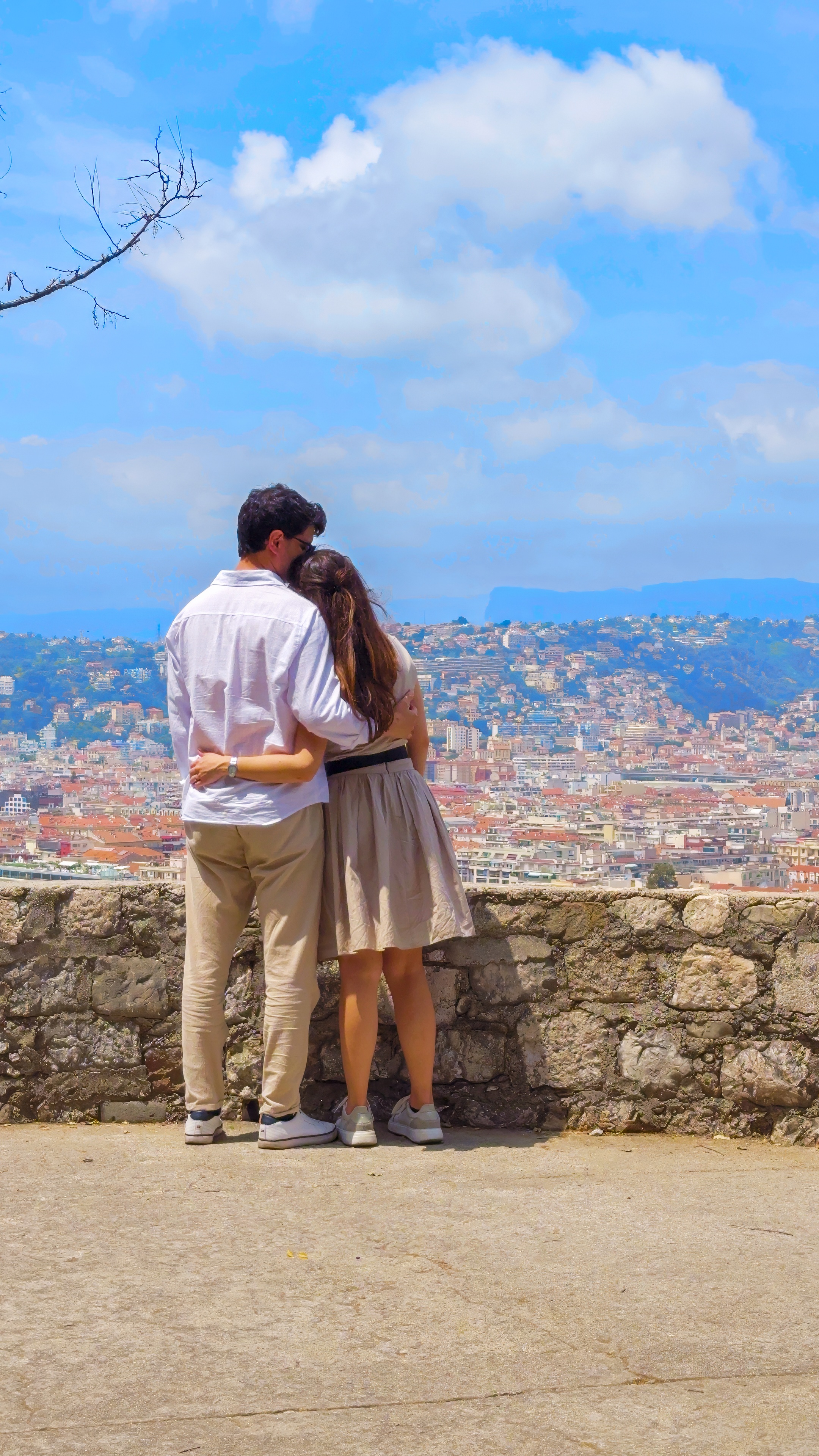 Davide and Barbara embracing by a stone wall, looking out over the roofs of the city and the hills.