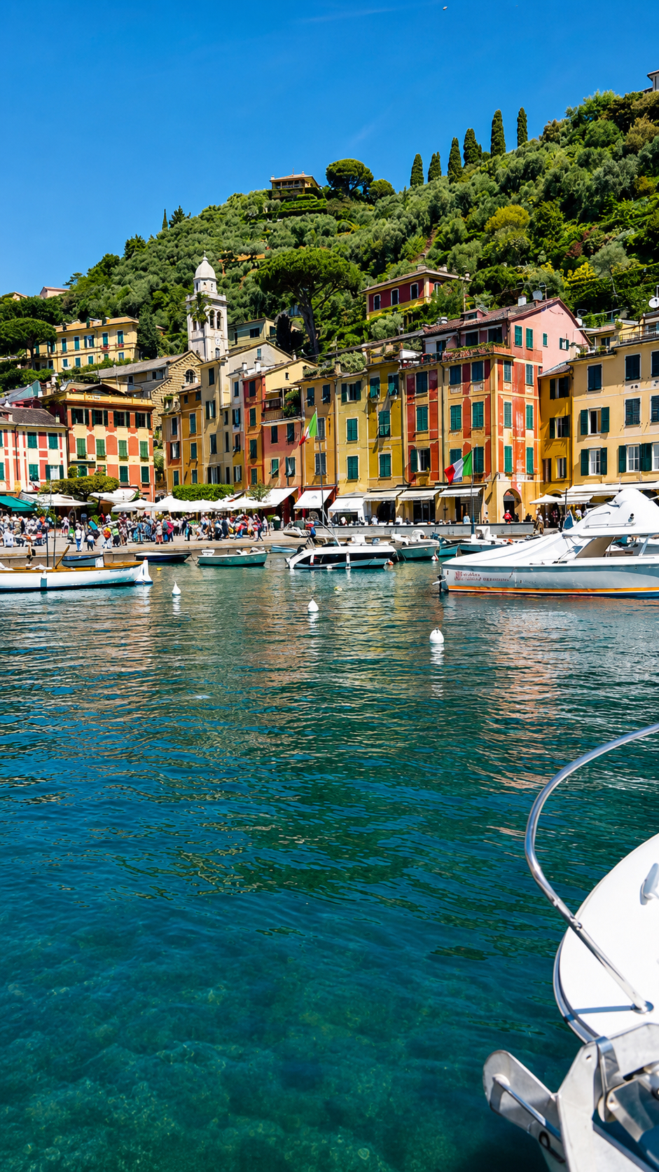 Tall painted houses along a harbour, with boats moored on clear green water.