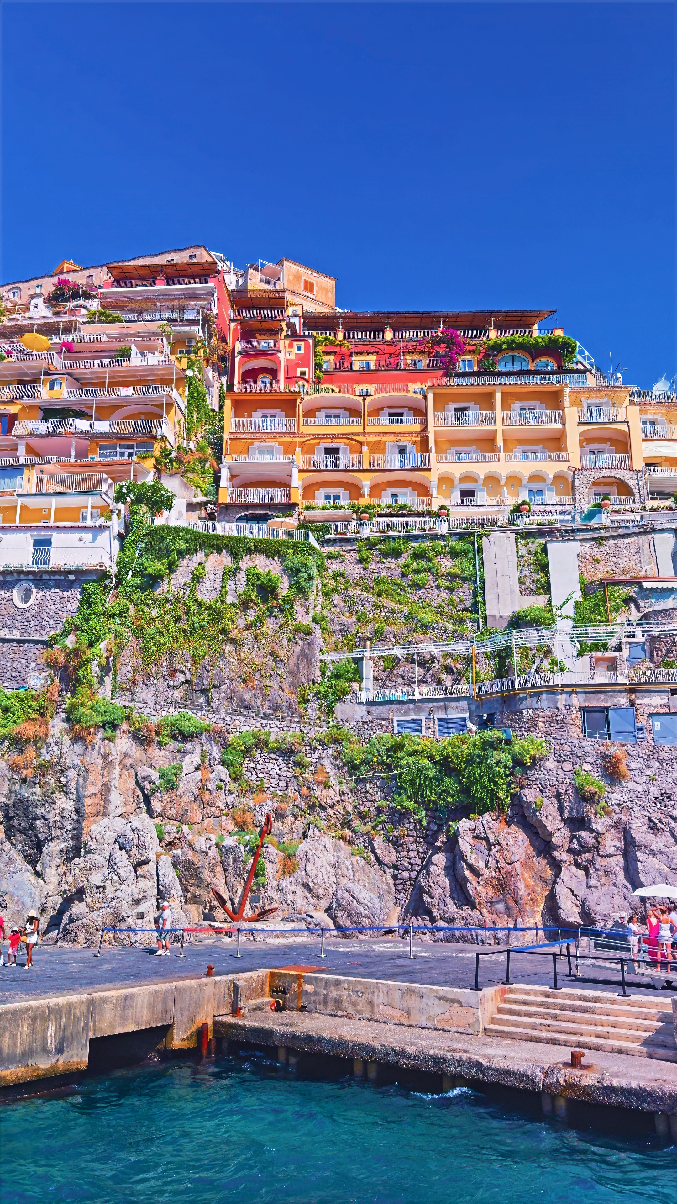 Pink and orange houses on a cliff above a small landing with steps down to the sea.