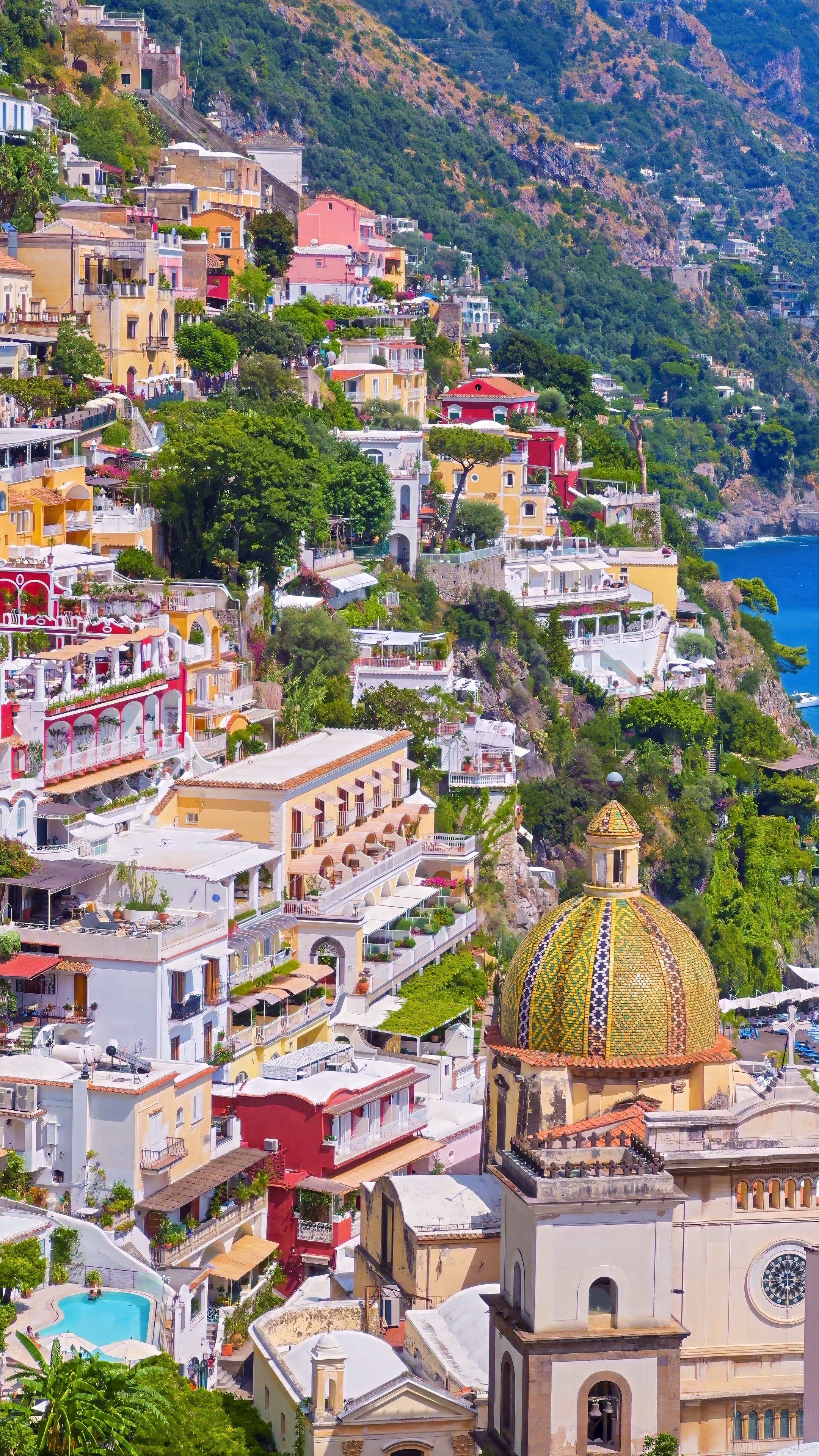 The majolica-tiled dome and bell tower of a church below terraces of pastel houses, seen from above.