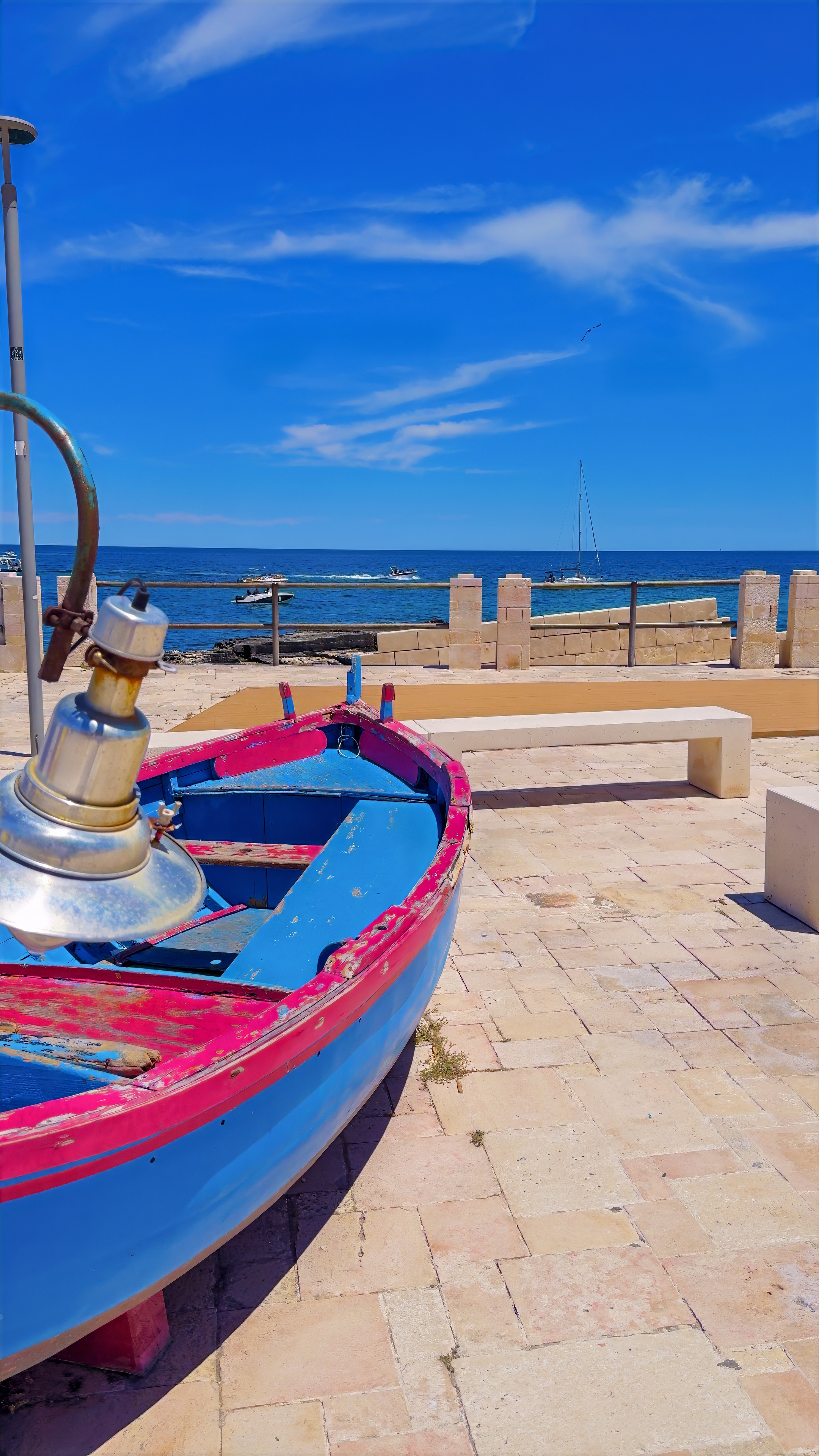 A blue wooden fishing boat pulled up on a small beach below old stone walls.