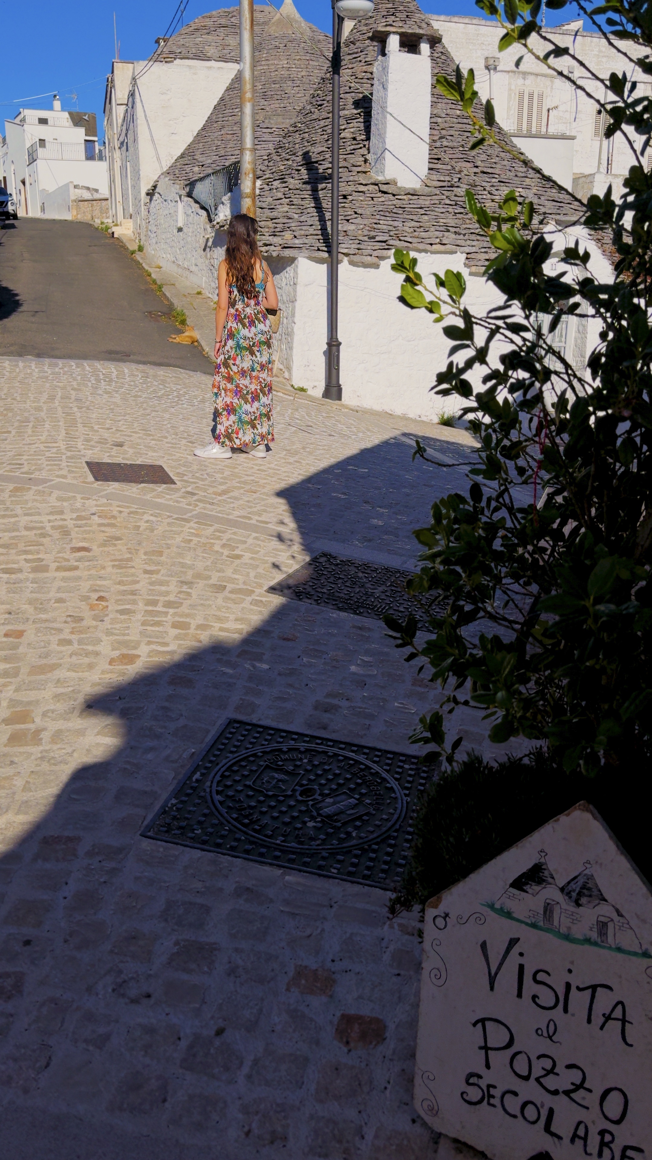 Barbara walking up a sloping stone lane between trulli with conical stone roofs.