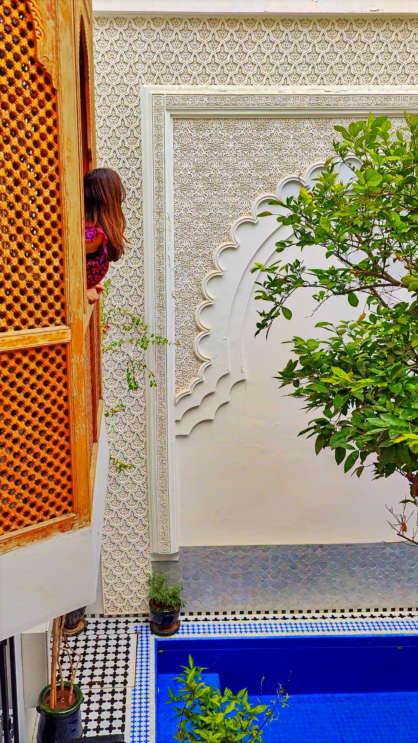 Carved white plaster around a wooden window screen, with the courtyard pool below