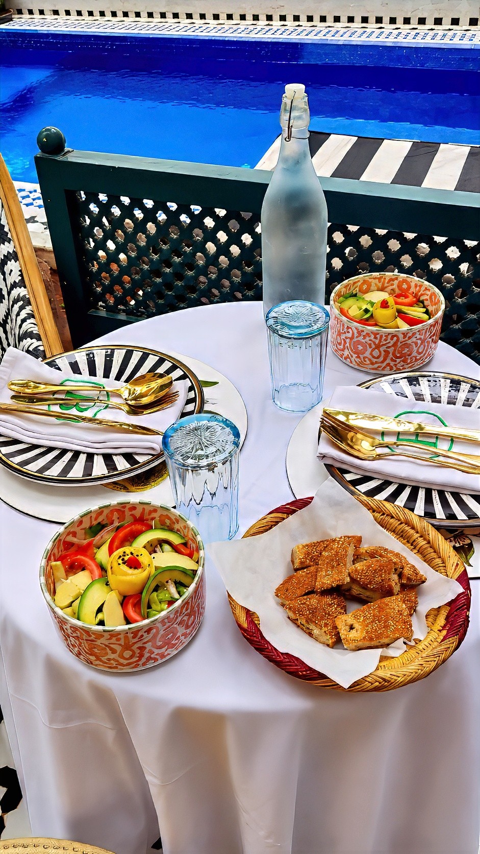 Lunch on a white tablecloth: salads, a basket of small fried bites and water, with the pool behind