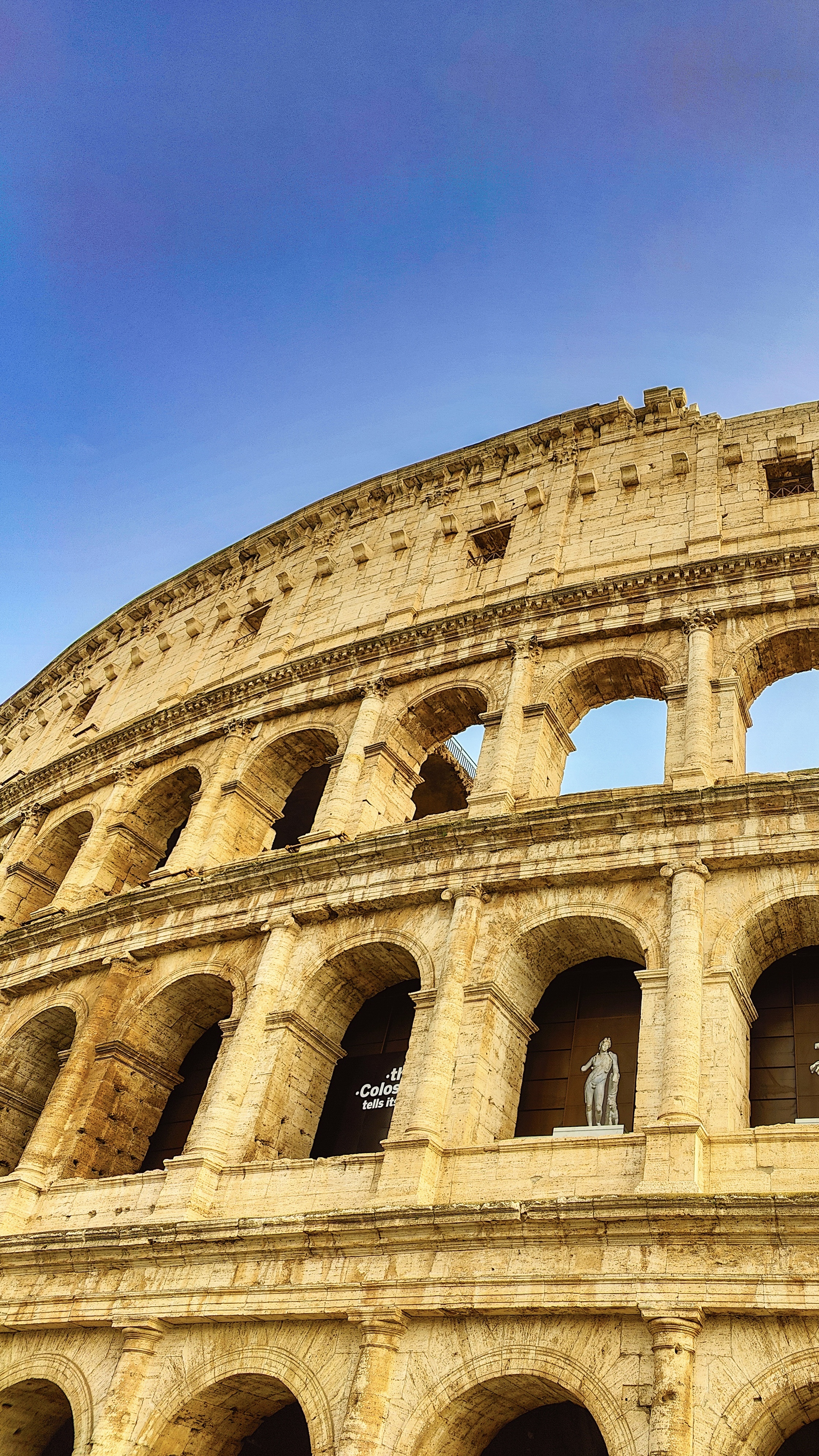 The upper arcades of the Colosseum against a blue sky