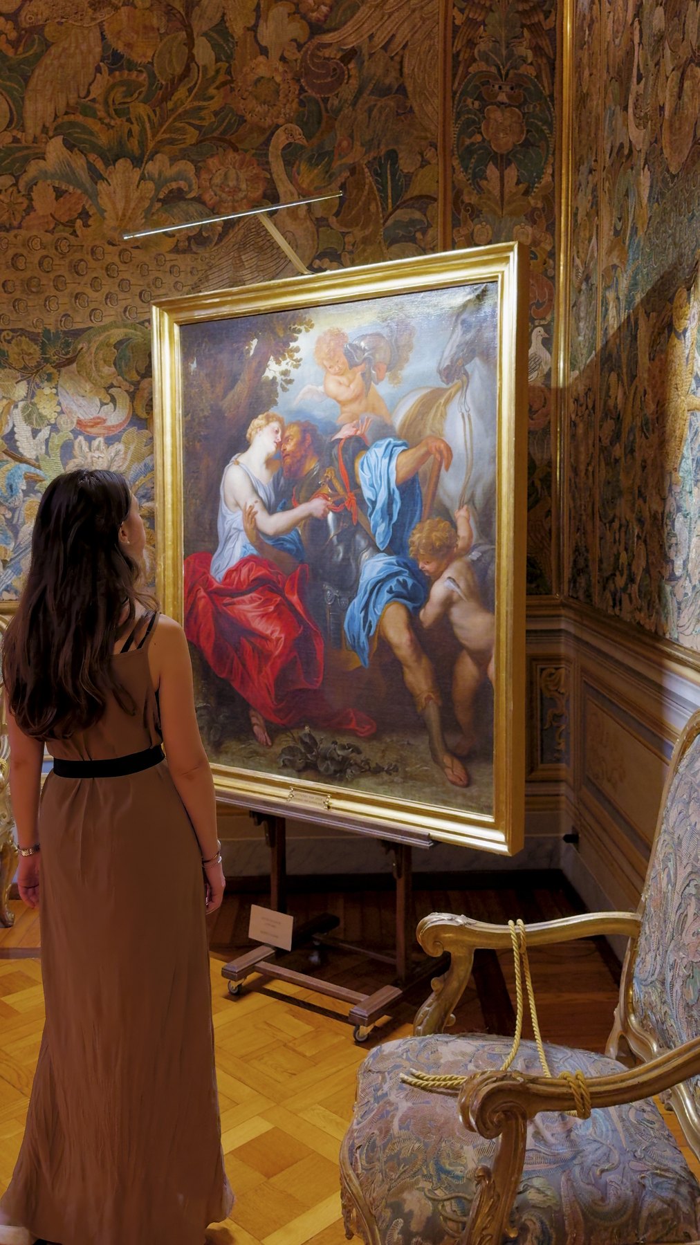 Barbara looking at a large framed painting on a red damask wall.