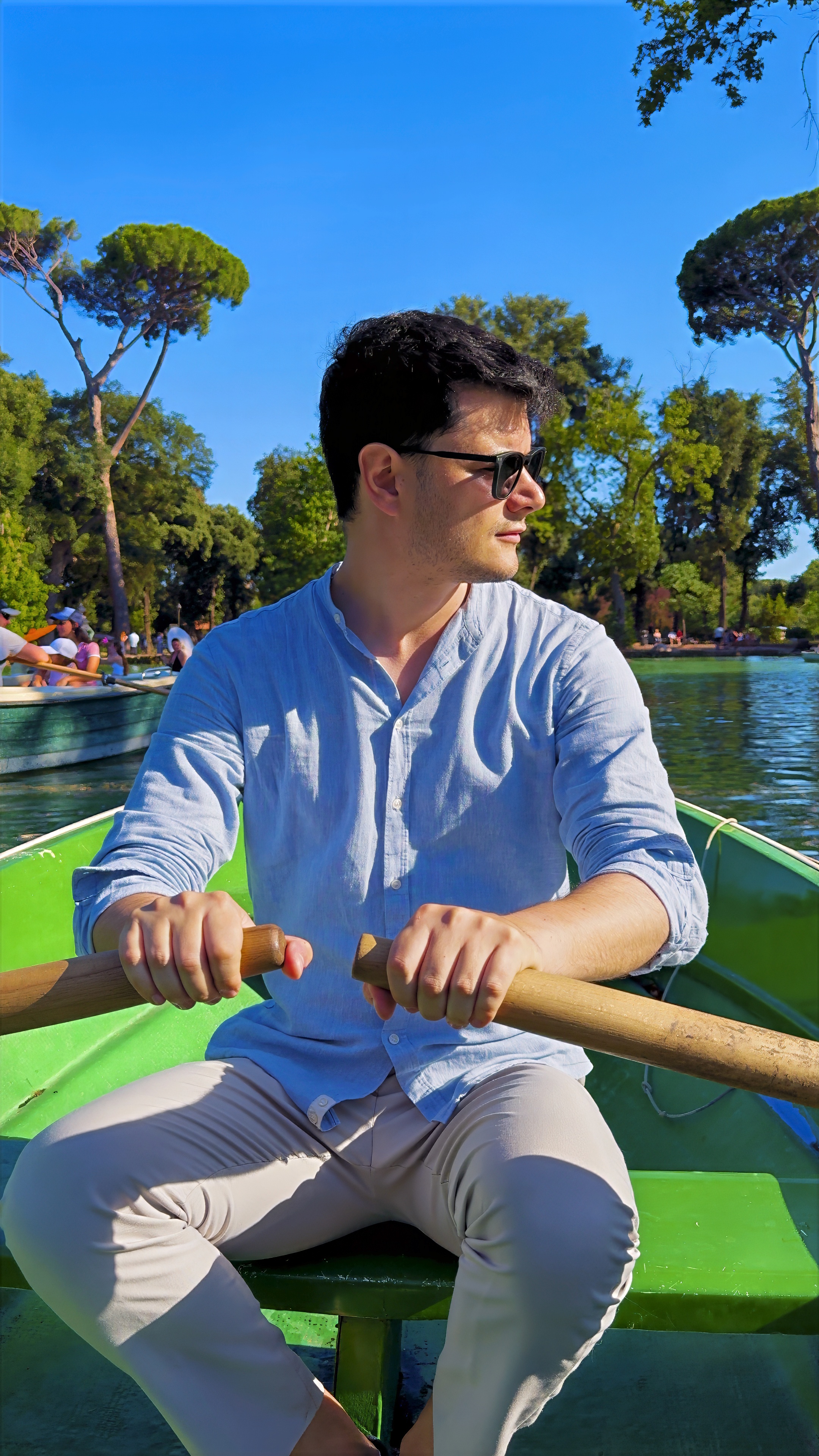 Davide rowing a green boat on a small lake, with trees on the shore behind.