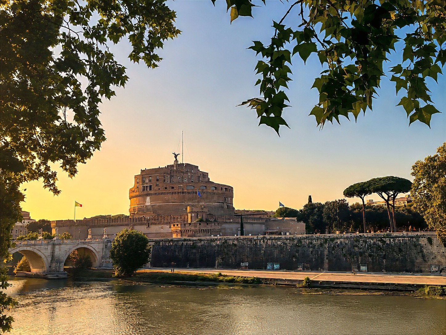 Castel Sant'Angelo and its bridge over the Tiber at sunset, framed by trees