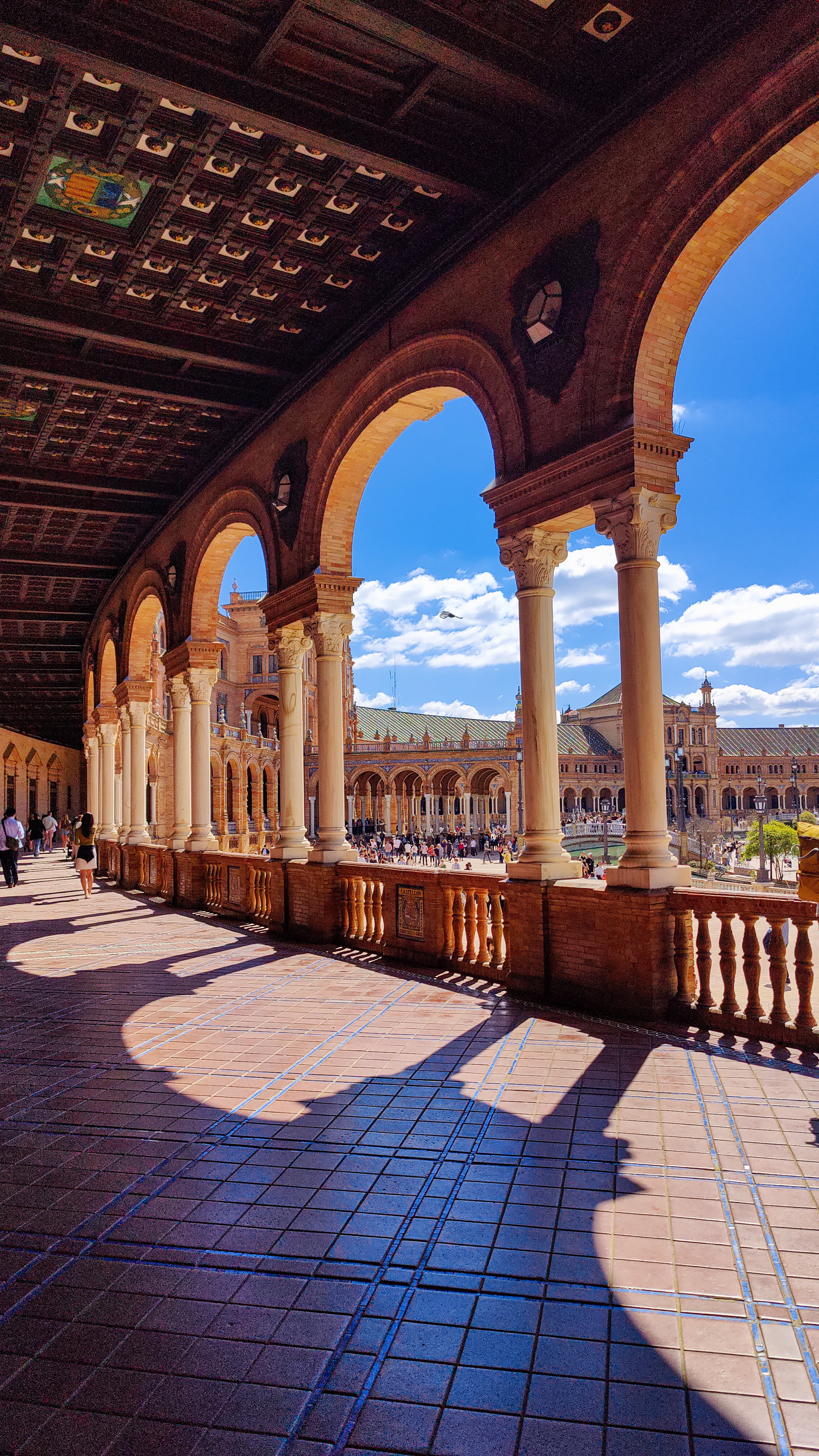 Sunlit brick arches and a tiled balustrade along the upper gallery of the Plaza de España