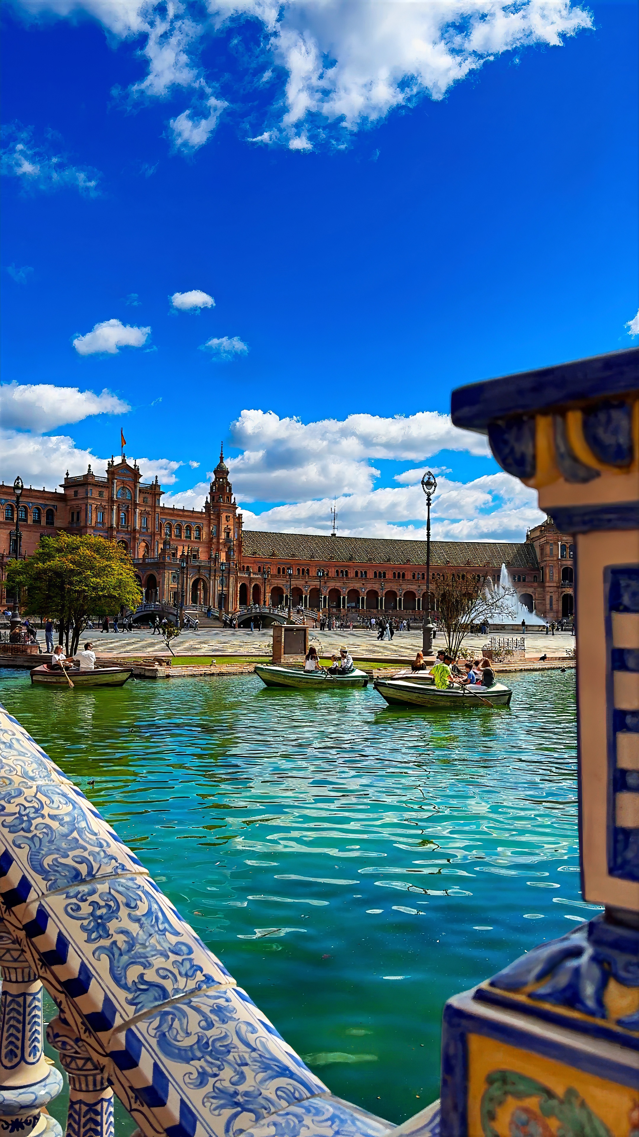 Rowing boats on the Plaza de España canal, seen past a blue-and-white tiled balustrade