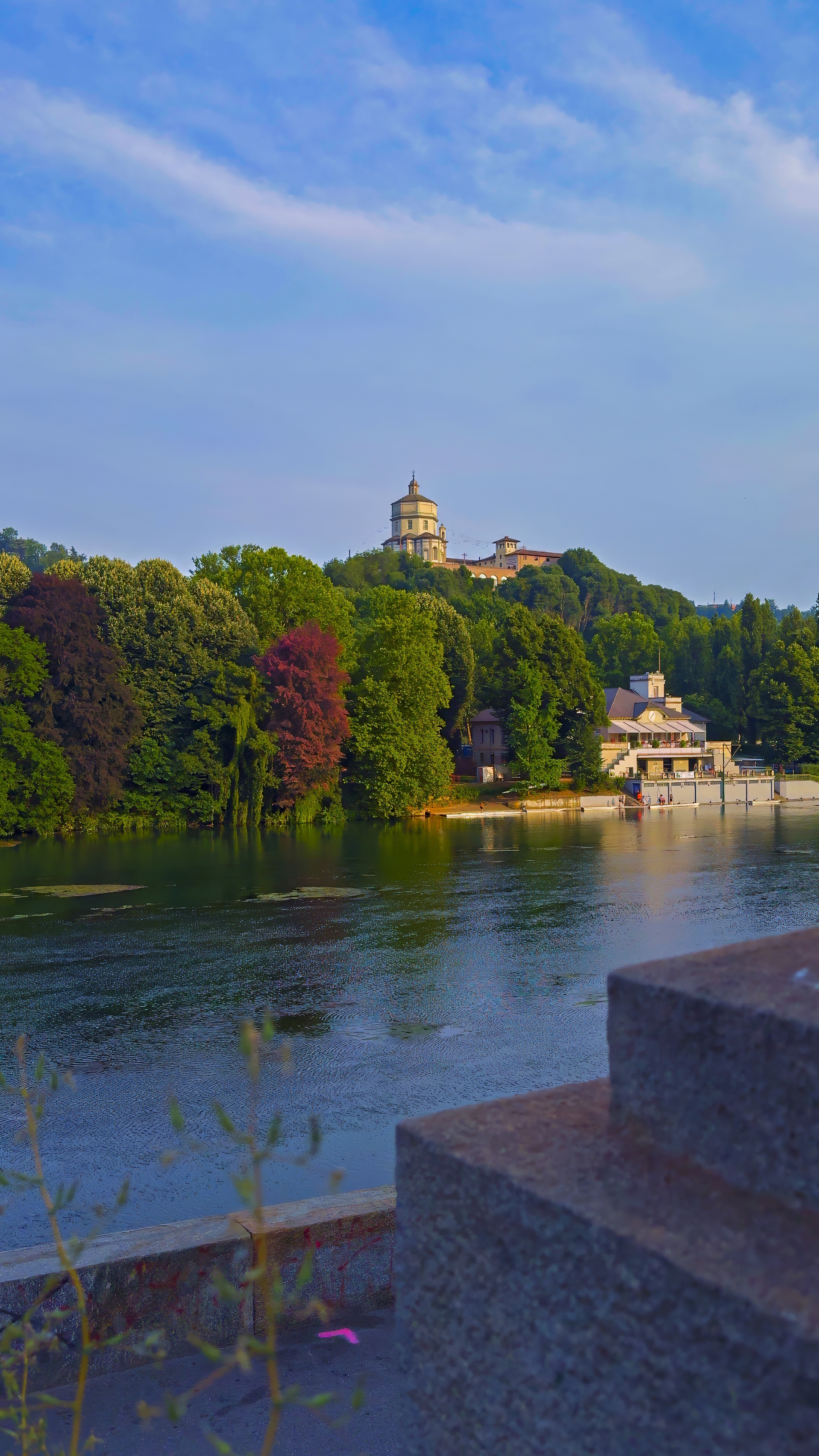 The Po lined with trees, with a church on the green hill above the river.