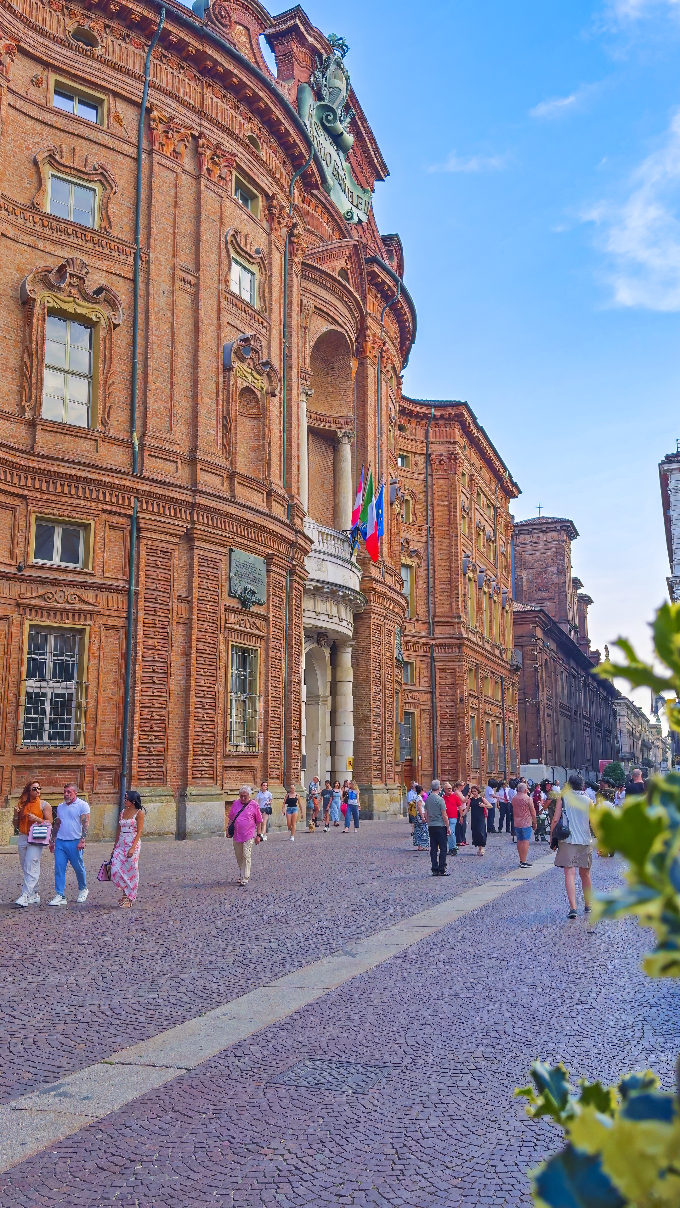 The curved red-brick façade of Palazzo Carignano, with people crossing the square.