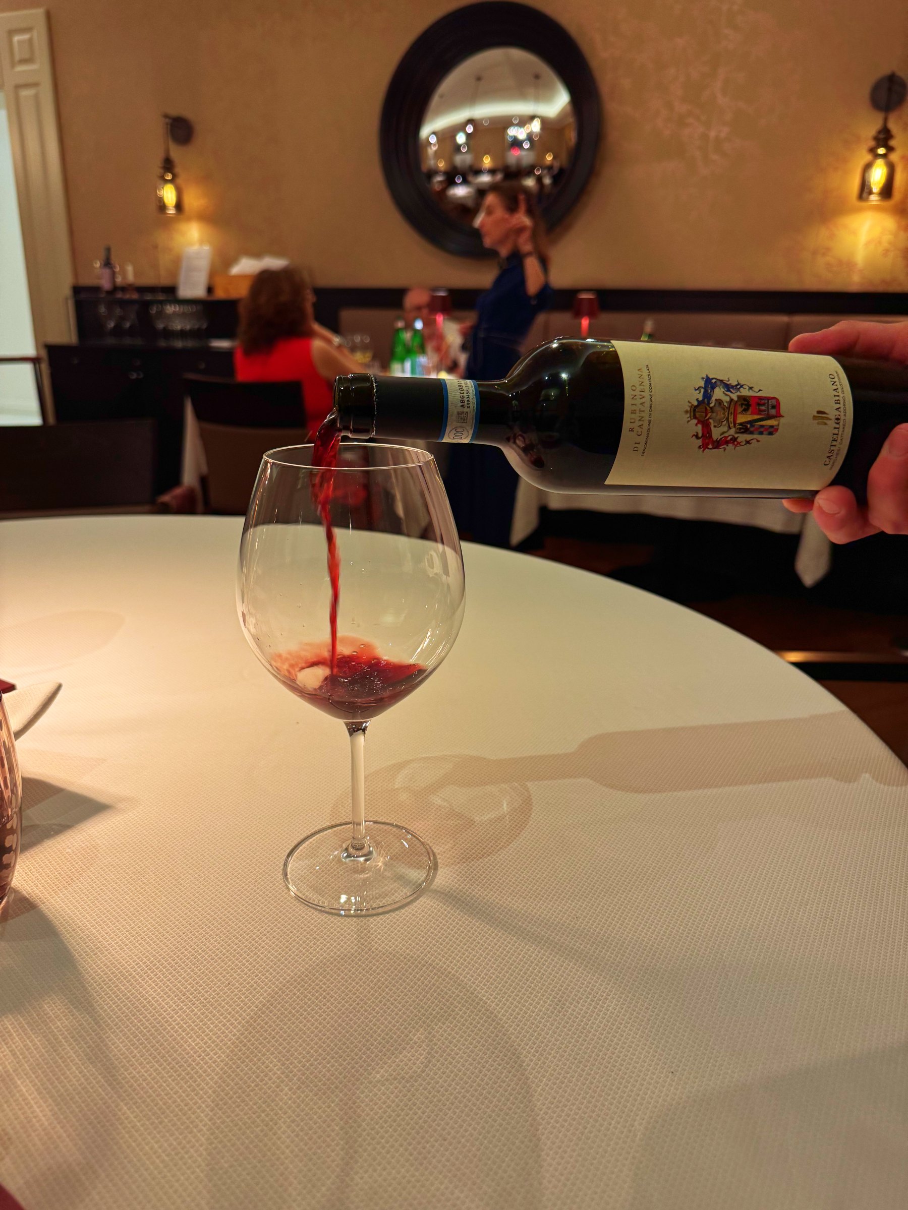 Red wine being poured into a glass on a white tablecloth at dinner