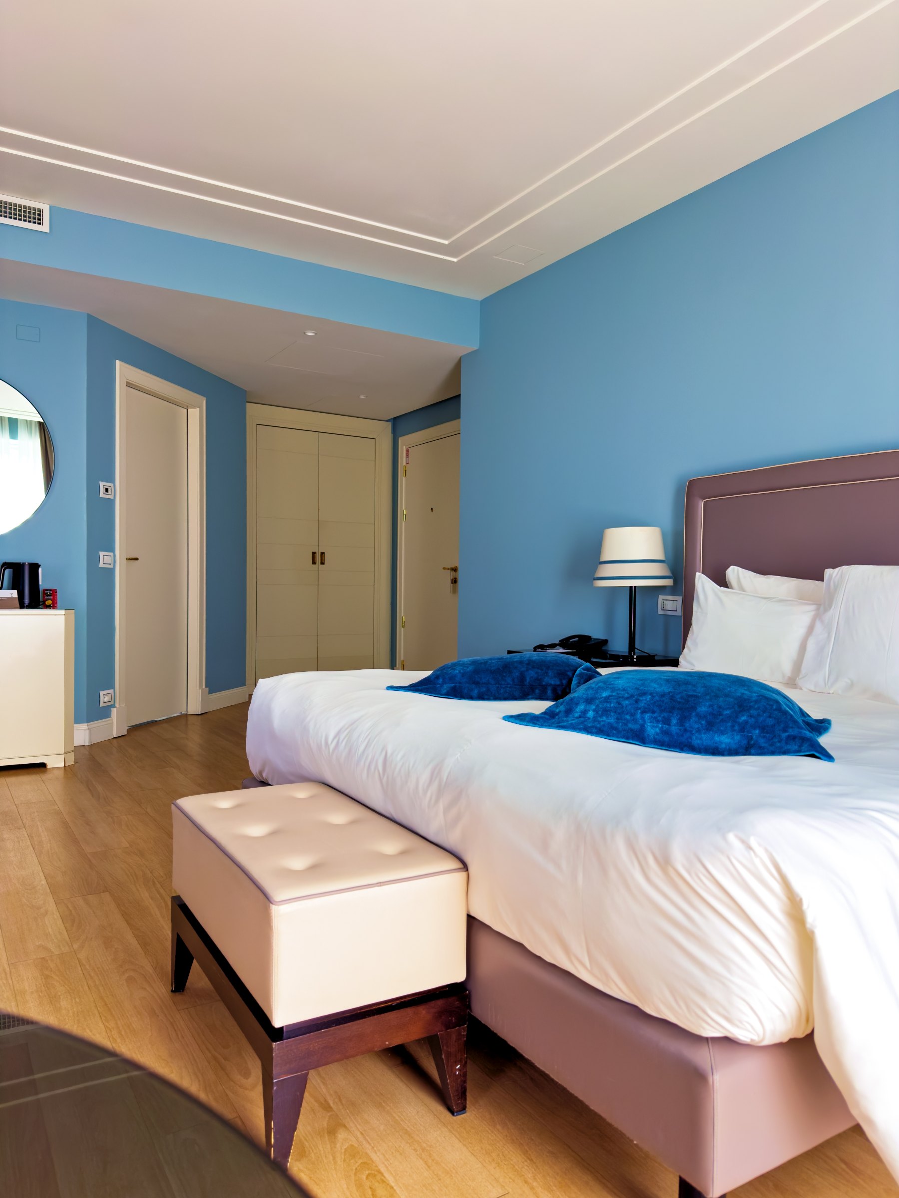 Our room: a white bed with a navy velvet runner and a footstool, pale blue walls and long curtains