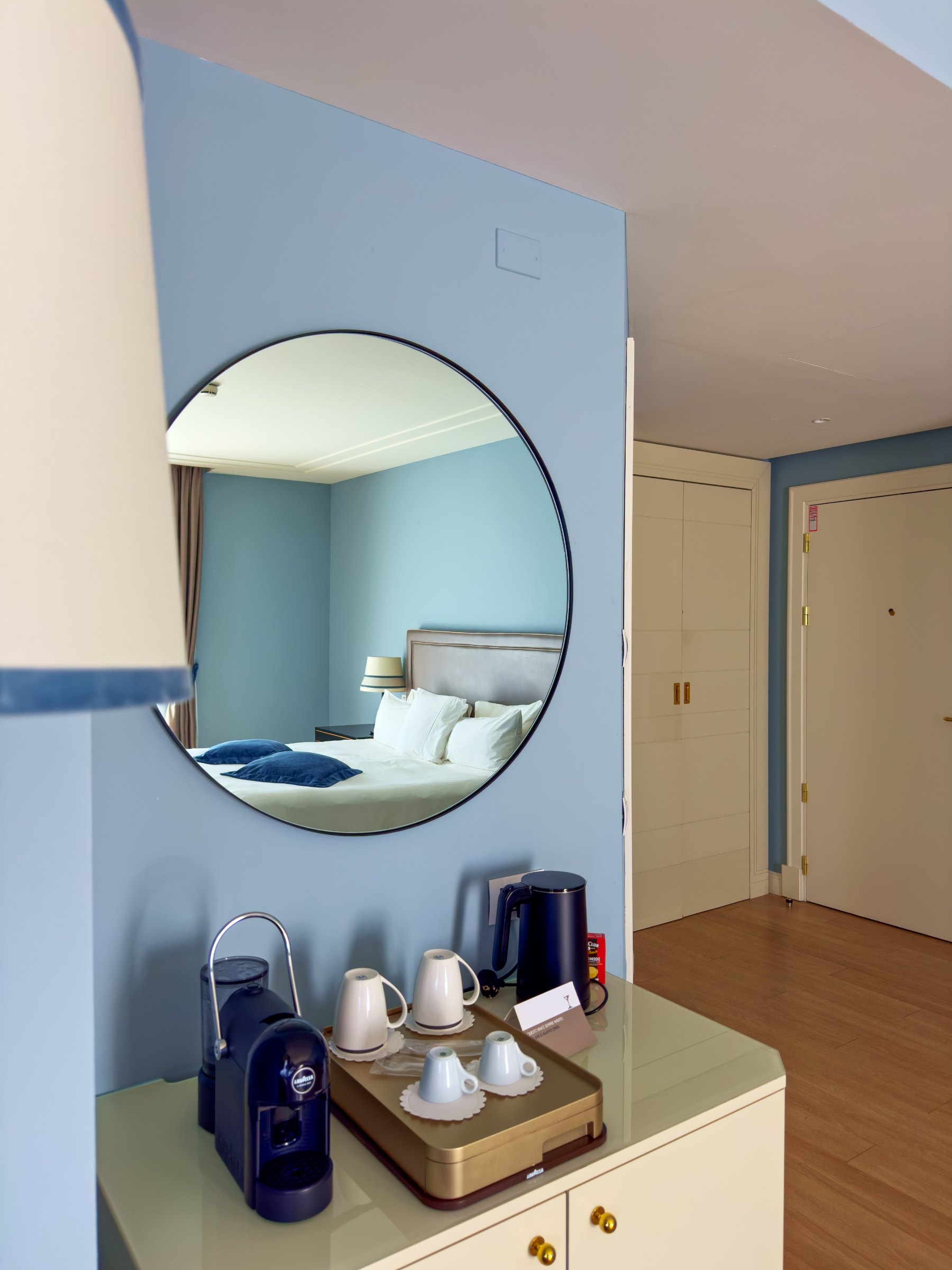 A round mirror on the pale blue wall above the coffee and tea tray in our room