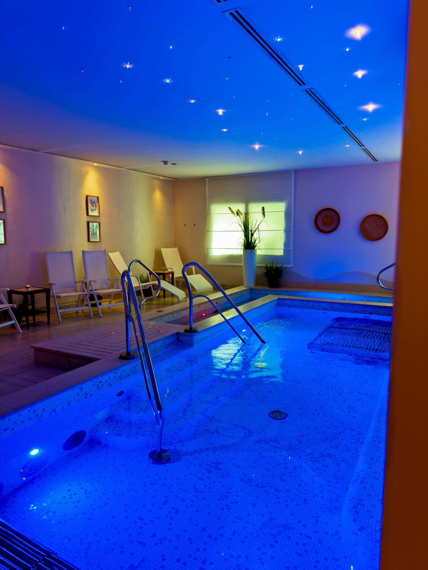 Blue-lit water in the hotel wellness area, with loungers along the side