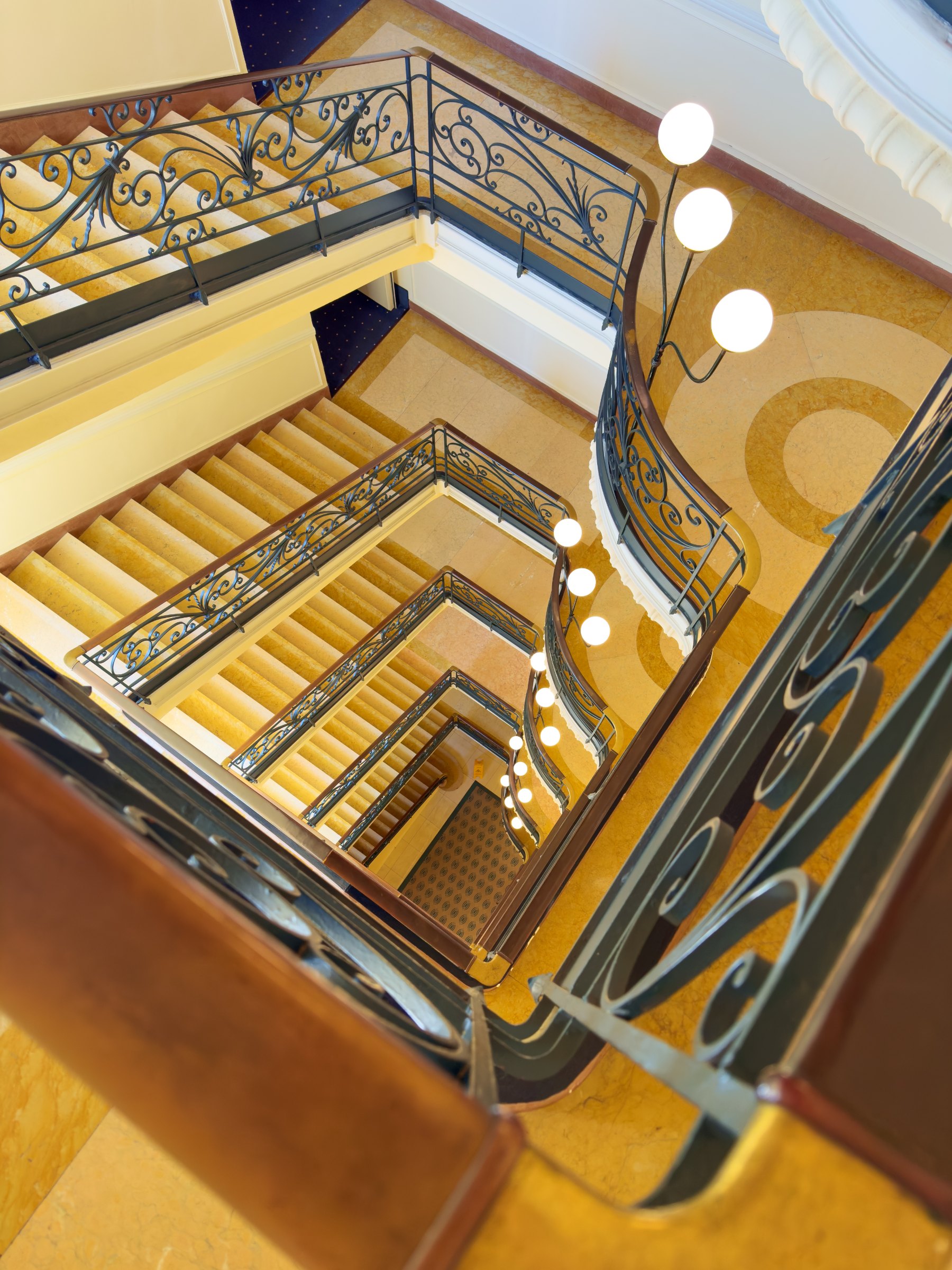 Looking down the hotel stairwell: a wrought-iron balustrade spiralling around warm stone steps