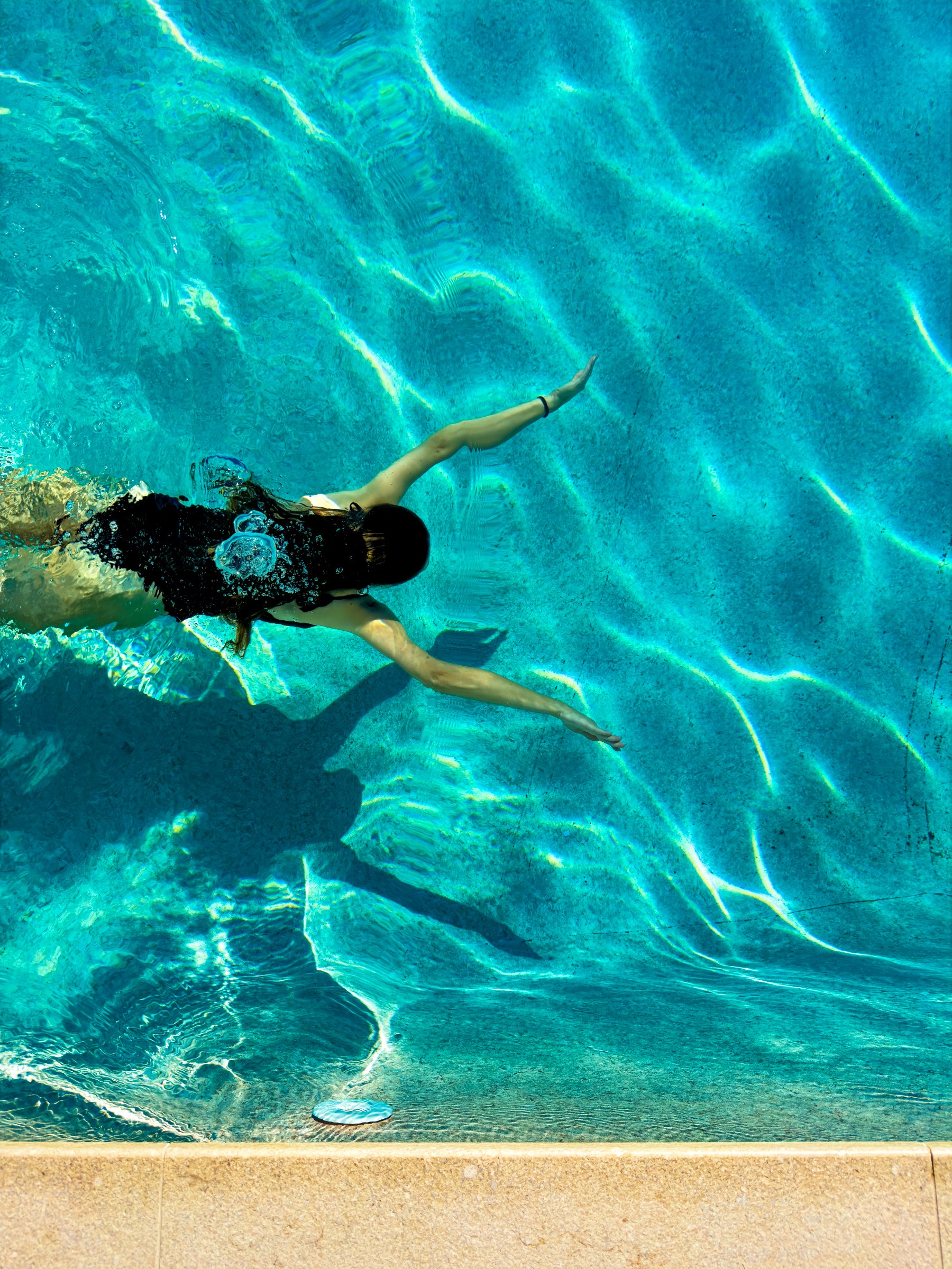 A swimmer seen from above in a turquoise pool, light rippling across the water