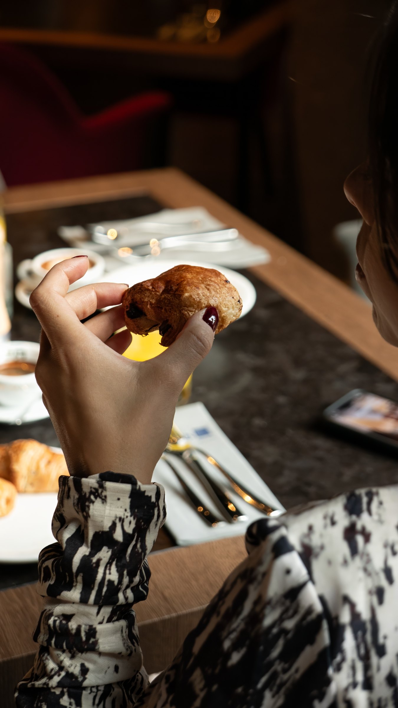 A hand holding a pain au chocolat over a breakfast table